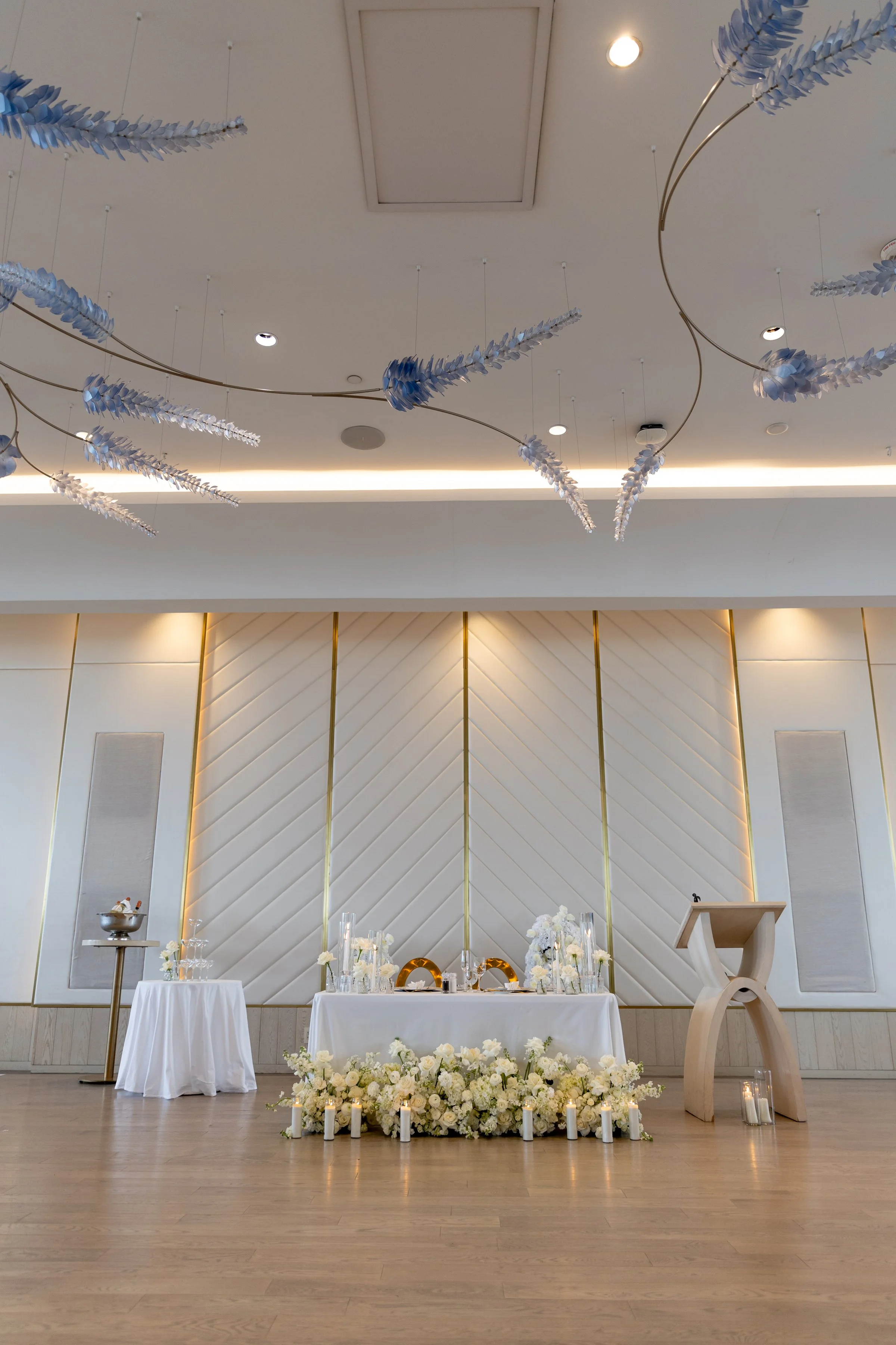 Elegant wedding altar decorated with white flowers and candles, with hanging blue and white floral arrangements from the ceiling and modern decor in the background.