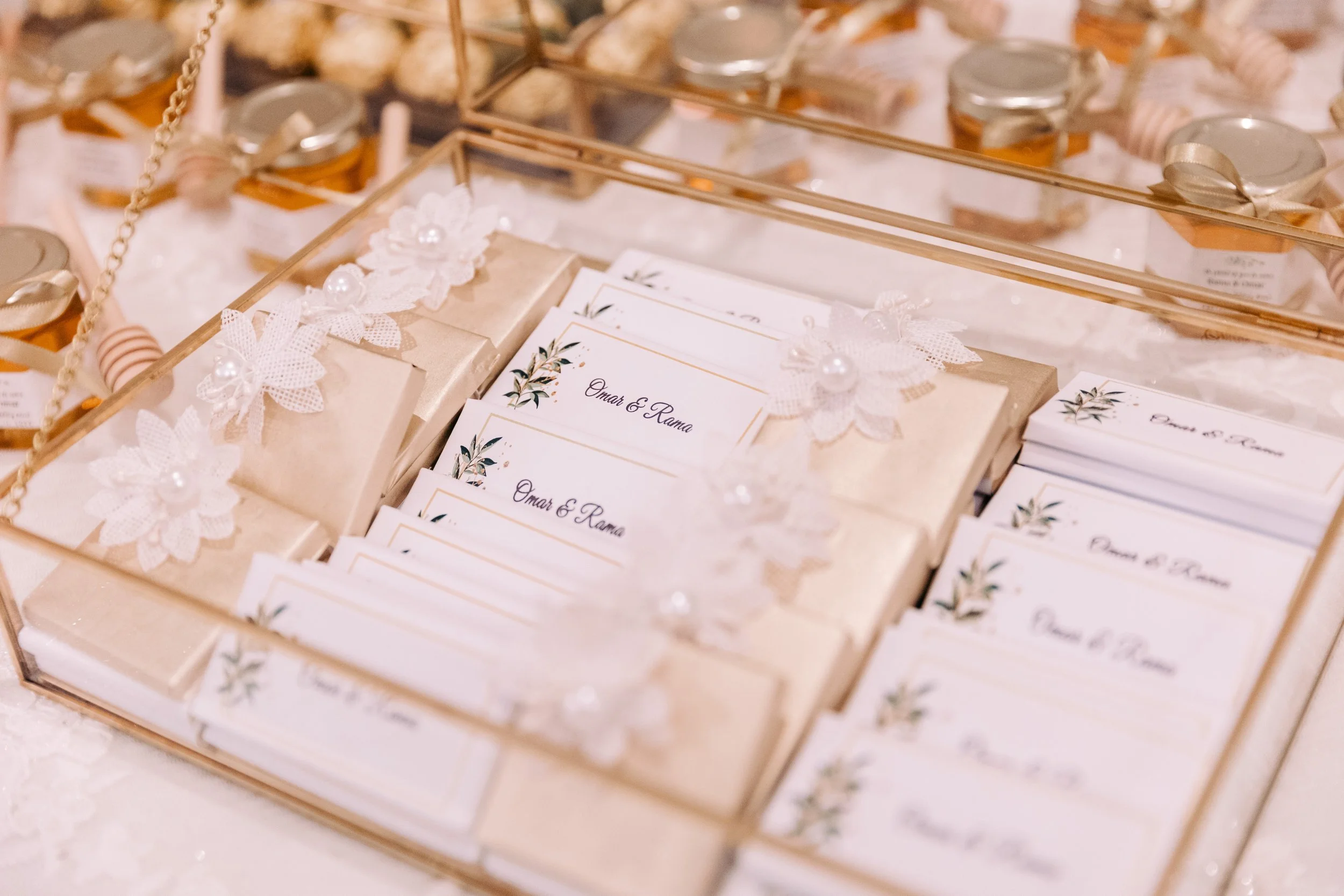 A display of wedding or event place cards and small gifts in a glass box decorated with white lace, flowers, and pearls.