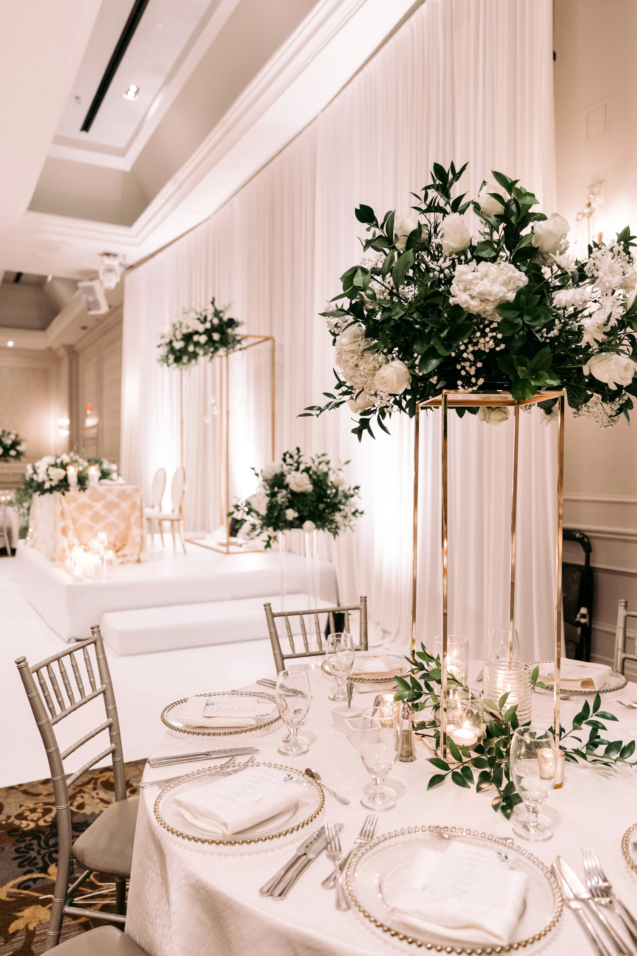 Elegant wedding reception table with white floral centerpieces and candle decorations in a decorated banquet hall.