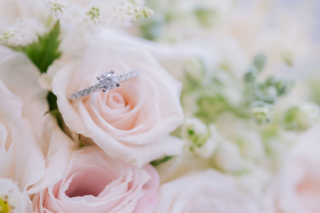 A diamond ring on a light pink rose among white roses and flowers.