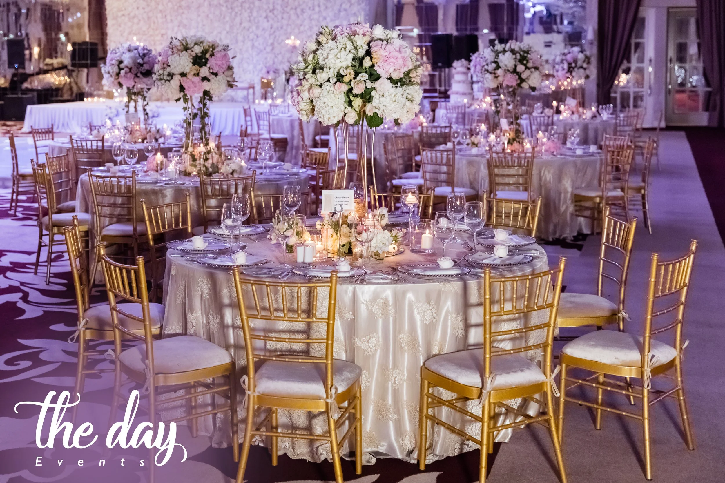 Elegant banquet hall decorated with floral centerpieces, gold Chiavari chairs, and candlelit tables, suitable for wedding reception or formal event.