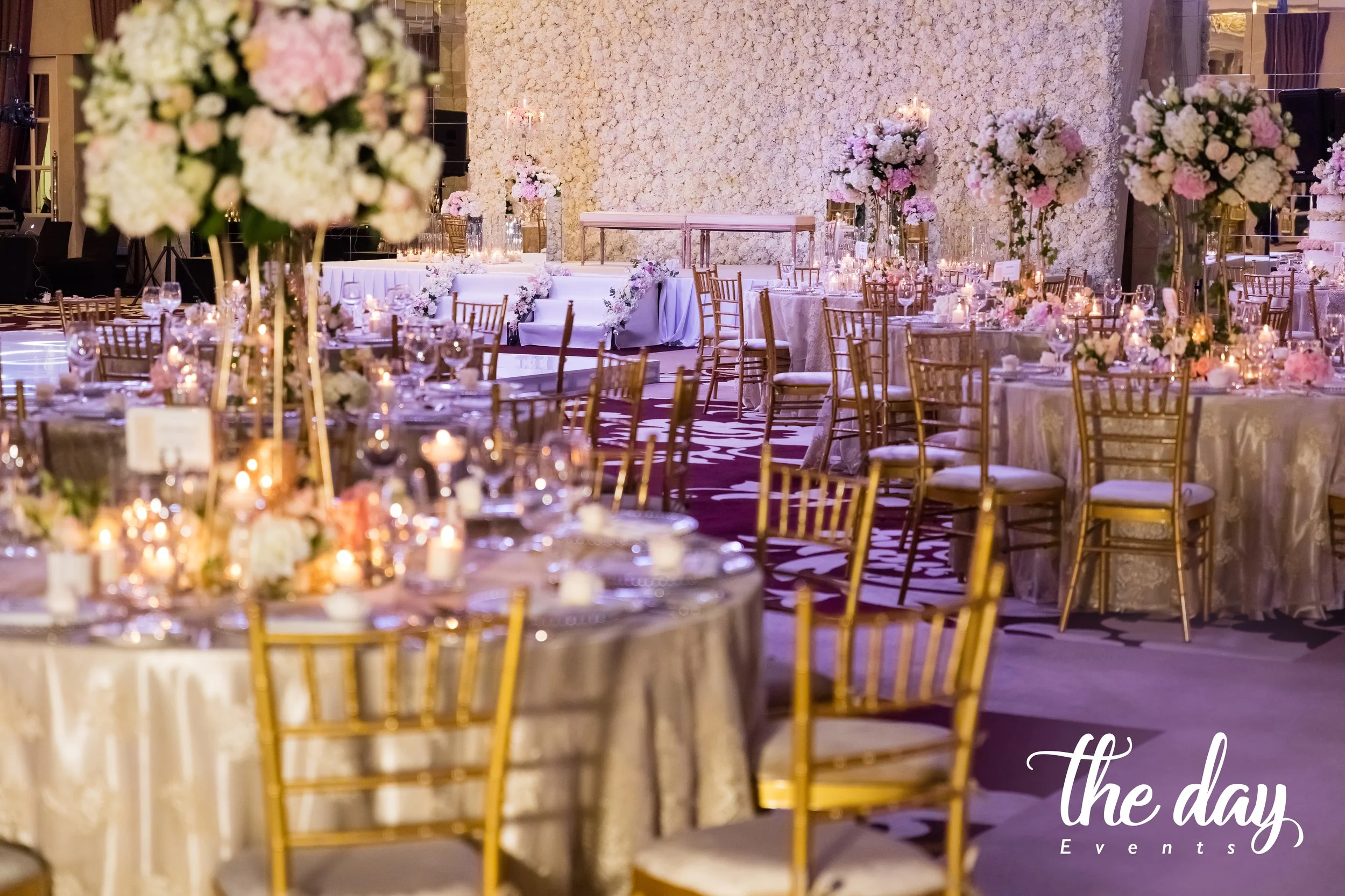 Elegant event space decorated with gold chairs, floral centerpieces, and candlelit tables in a ballroom setting.