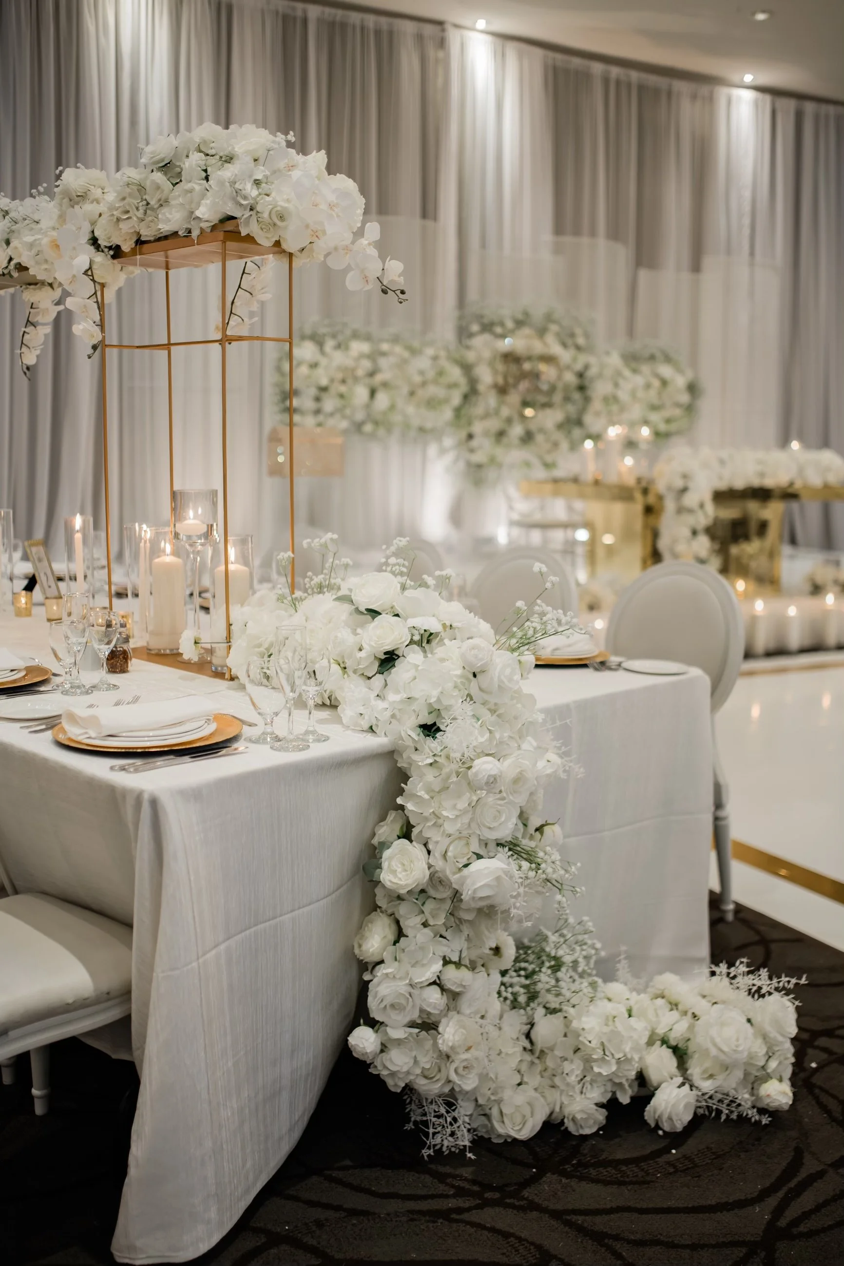 Elegant wedding reception table decorated with white flowers, candles, and gold accents in a luxurious setting.
