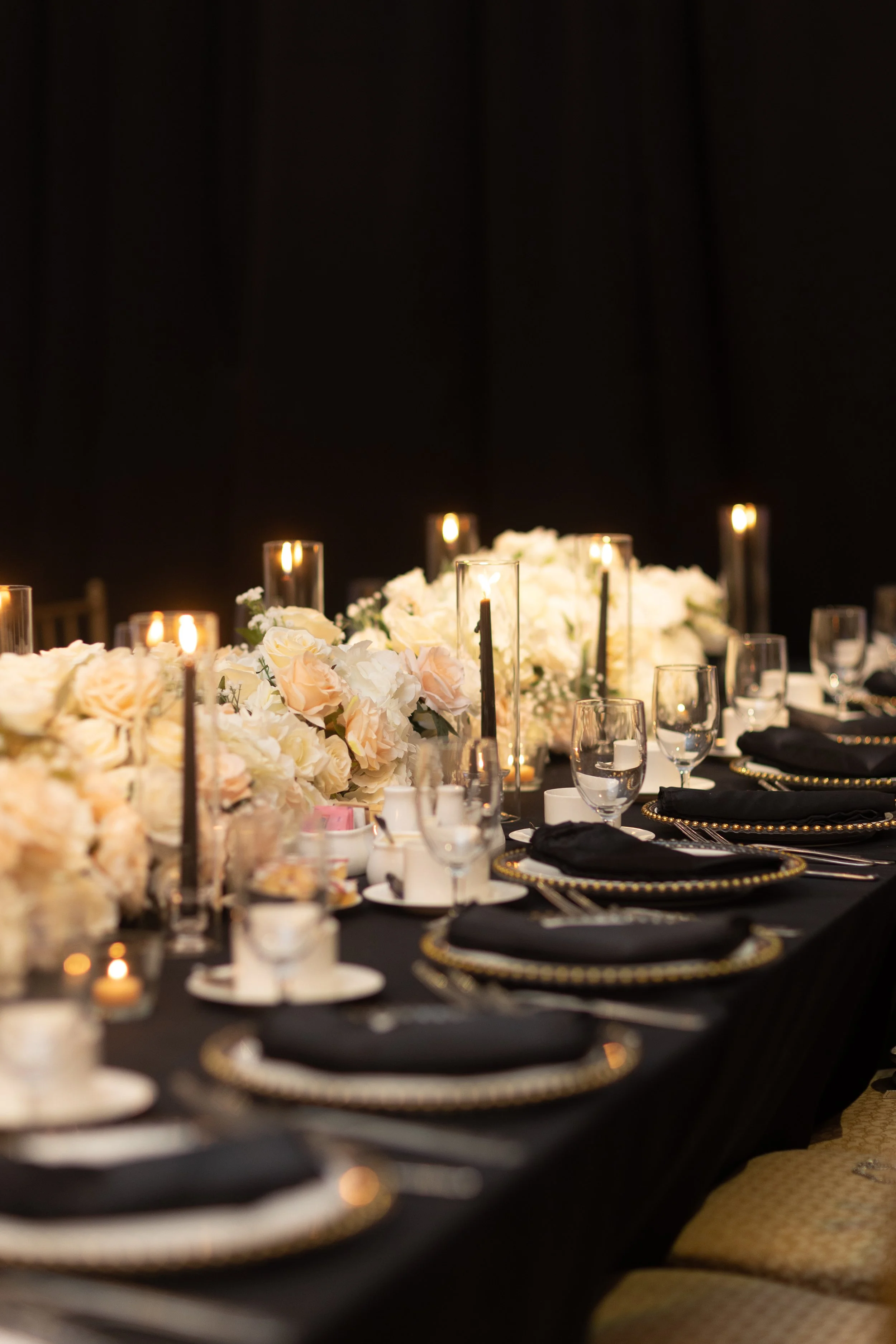 Elegant banquet table with black tablecloth, white floral centerpiece, black napkins, glassware, and lit candles.