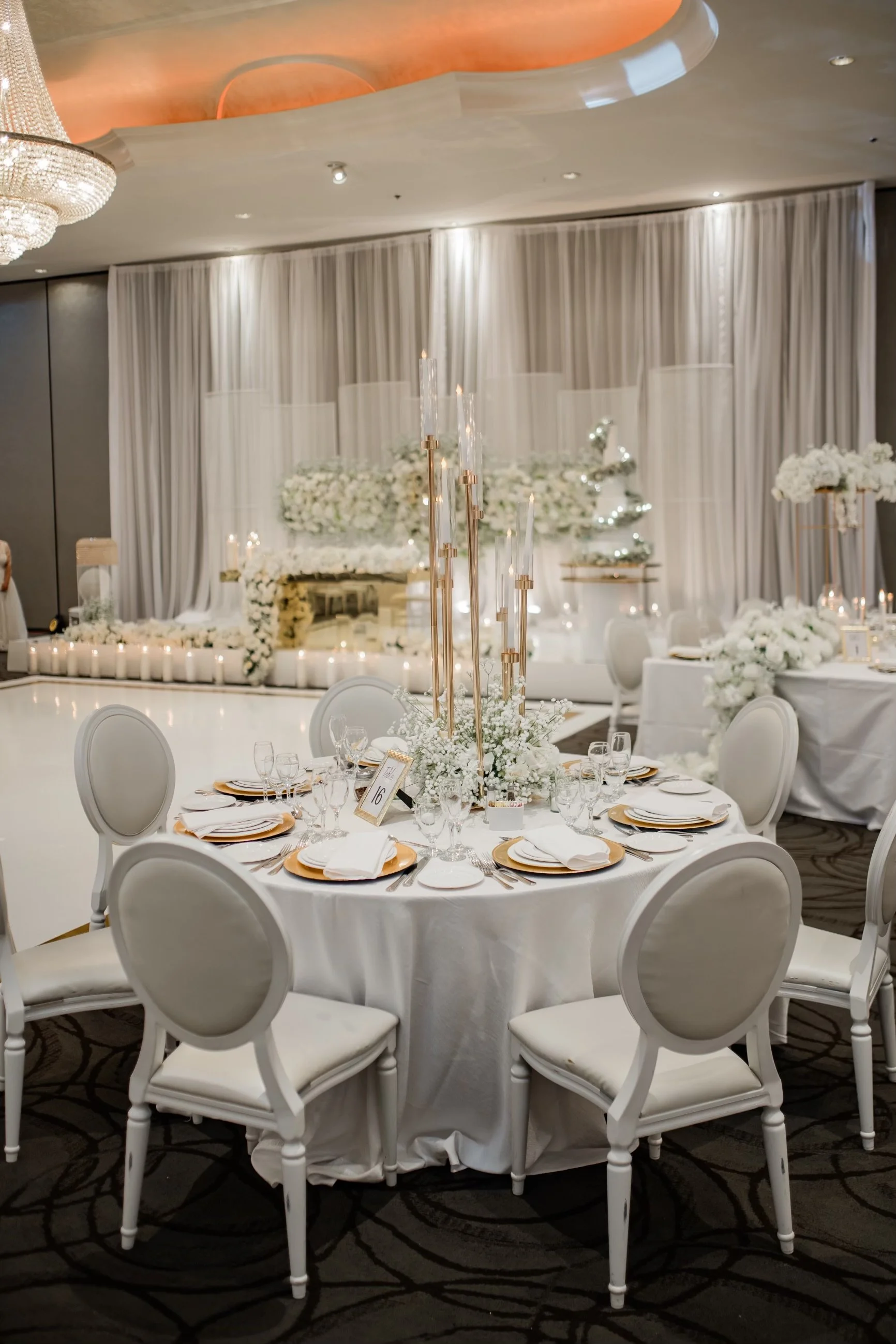 Elegant banquet table with white tablecloth, gold charger plates, and floral centerpieces, set for a wedding reception.