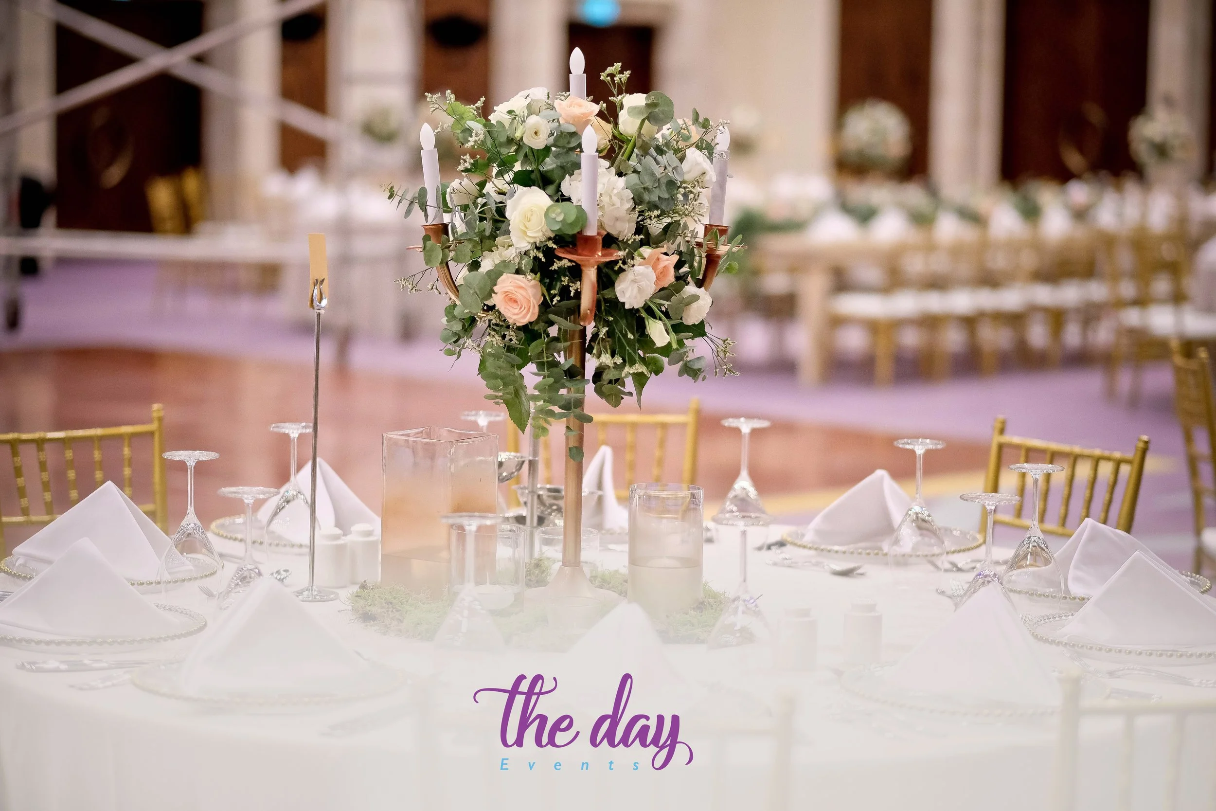 Elegant wedding reception table with a floral centerpiece, candles, and glassware, with a logo for 'the day Events' at the bottom.