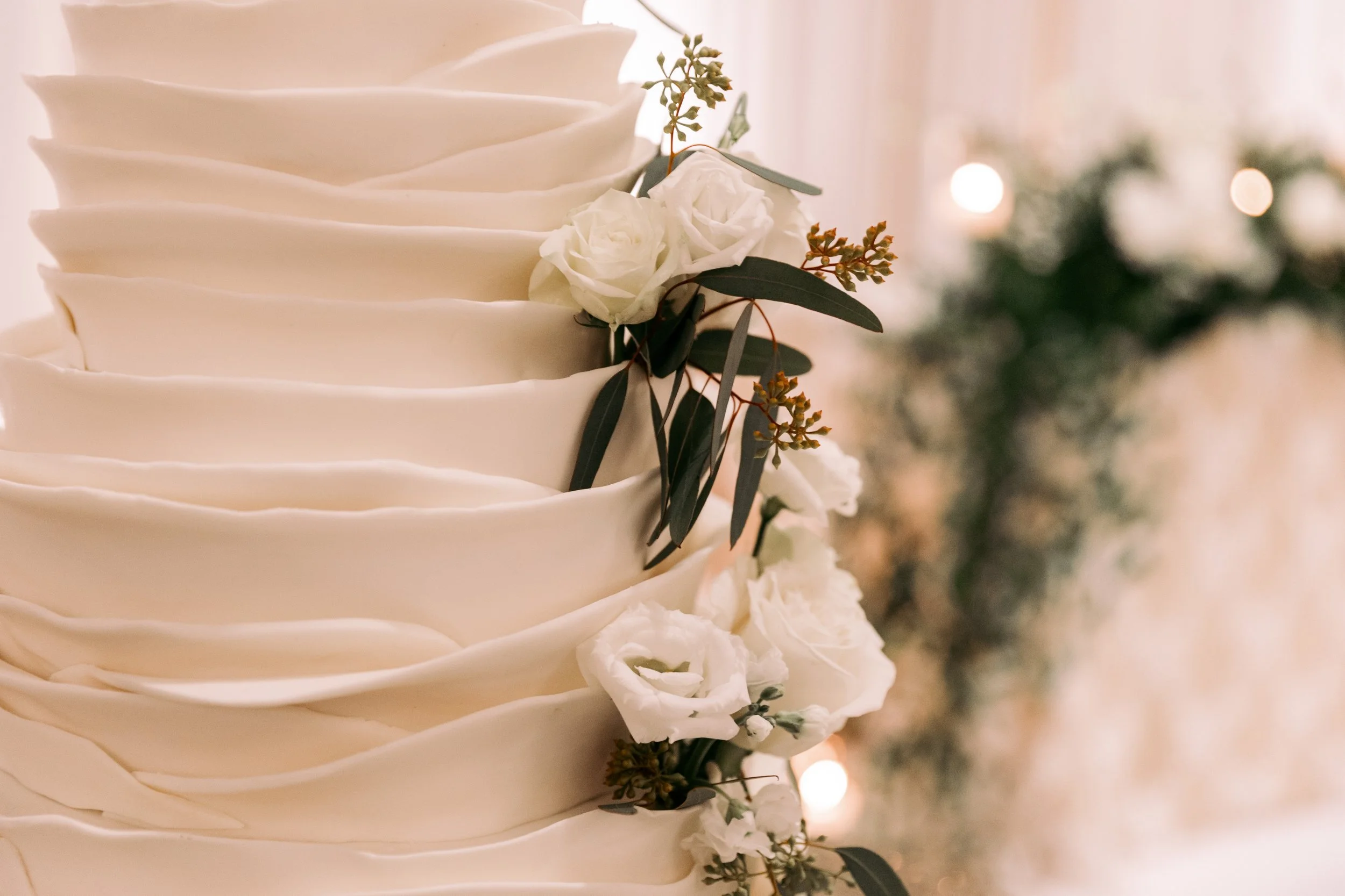 Close-up of a multi-layer white wedding cake decorated with white roses and greenery