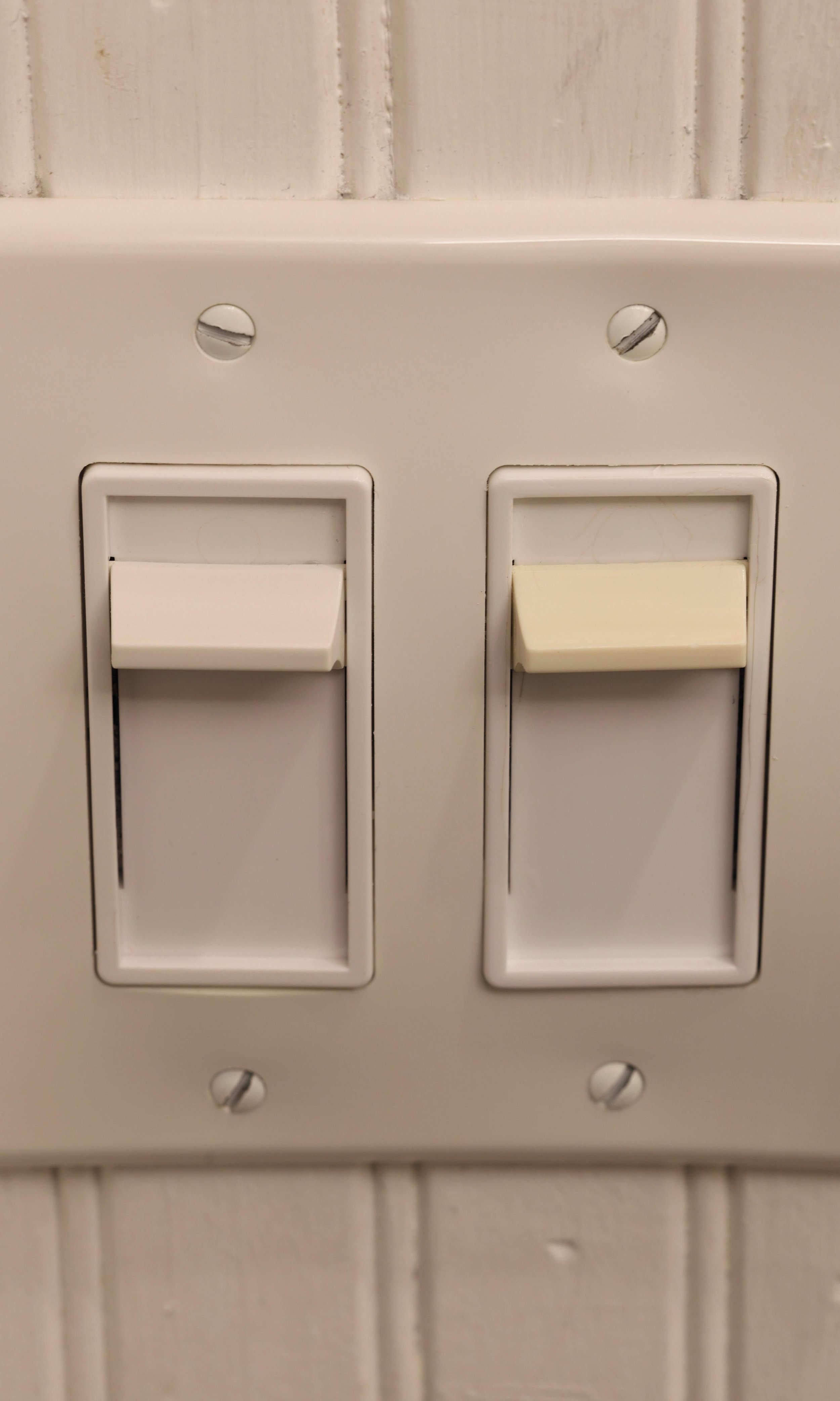 Two white rocker light switches on a wall with white brick background.