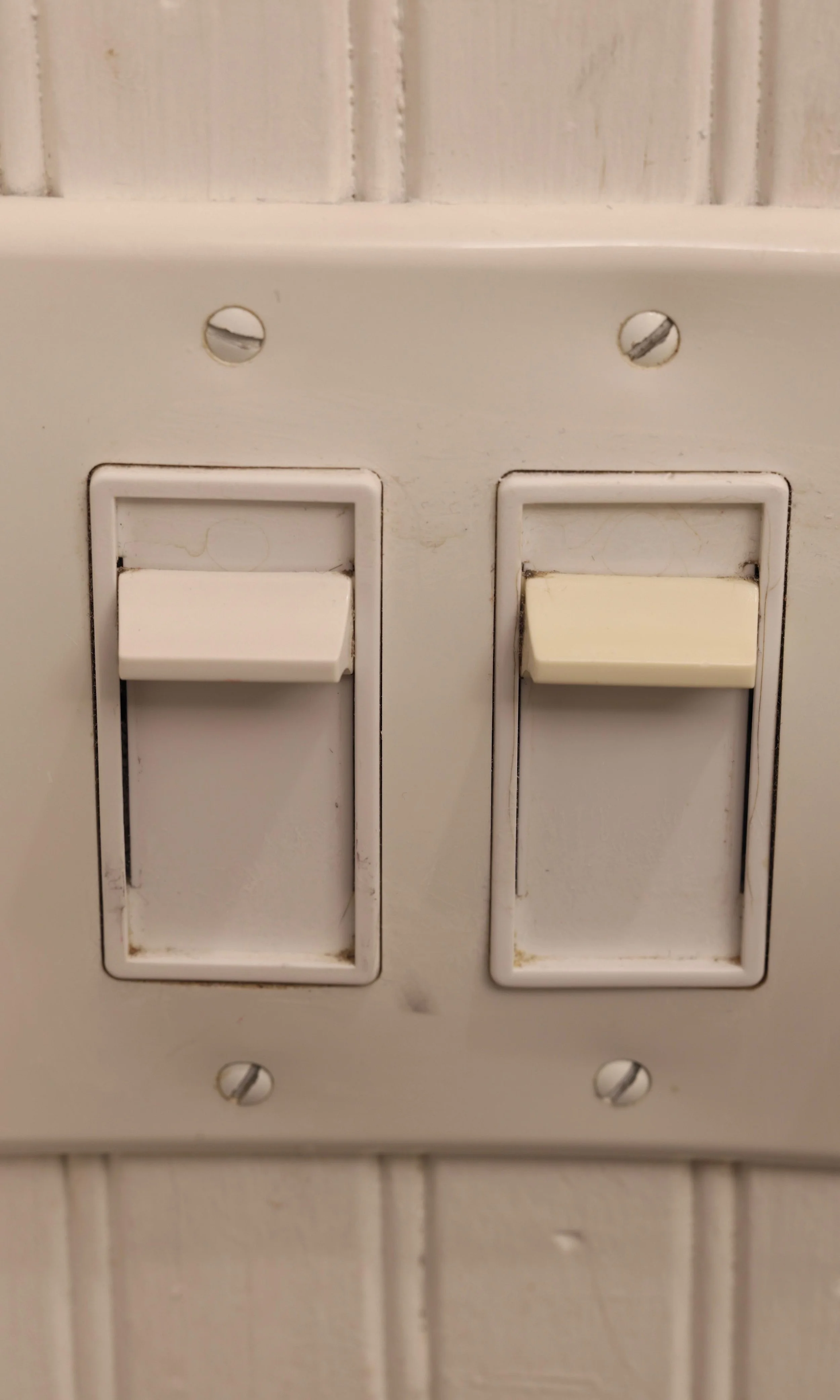 A close-up of two white light switches on a wall with visible dirt and grime.