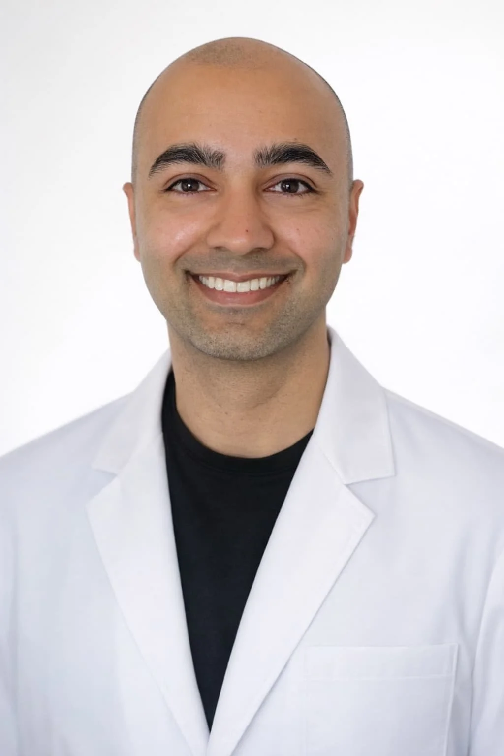 Professional headshot of a smiling man with a shaved head, wearing a white lab coat and a black shirt against a plain white background.