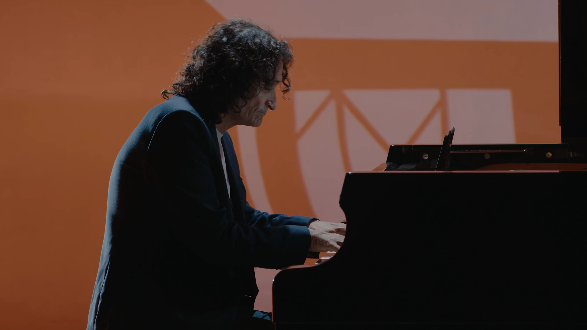 Homme jouant du piano sur scène avec un fond orange