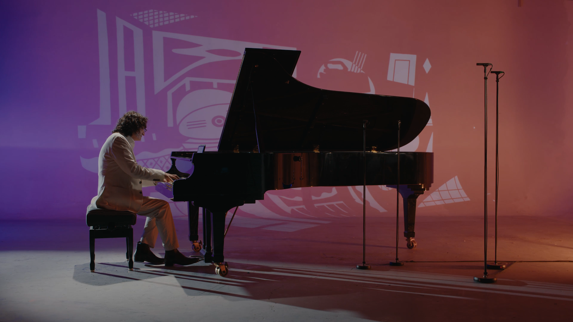 Un homme joue du piano noir sur scène, avec un fond lumineux coloré et un micro à proximité.