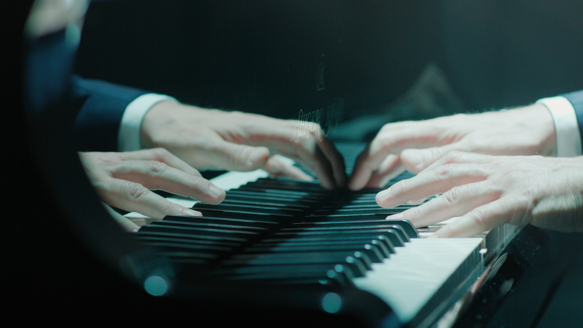 Mains de deux personnes jouant du piano sur un clavier noir et blanc.
