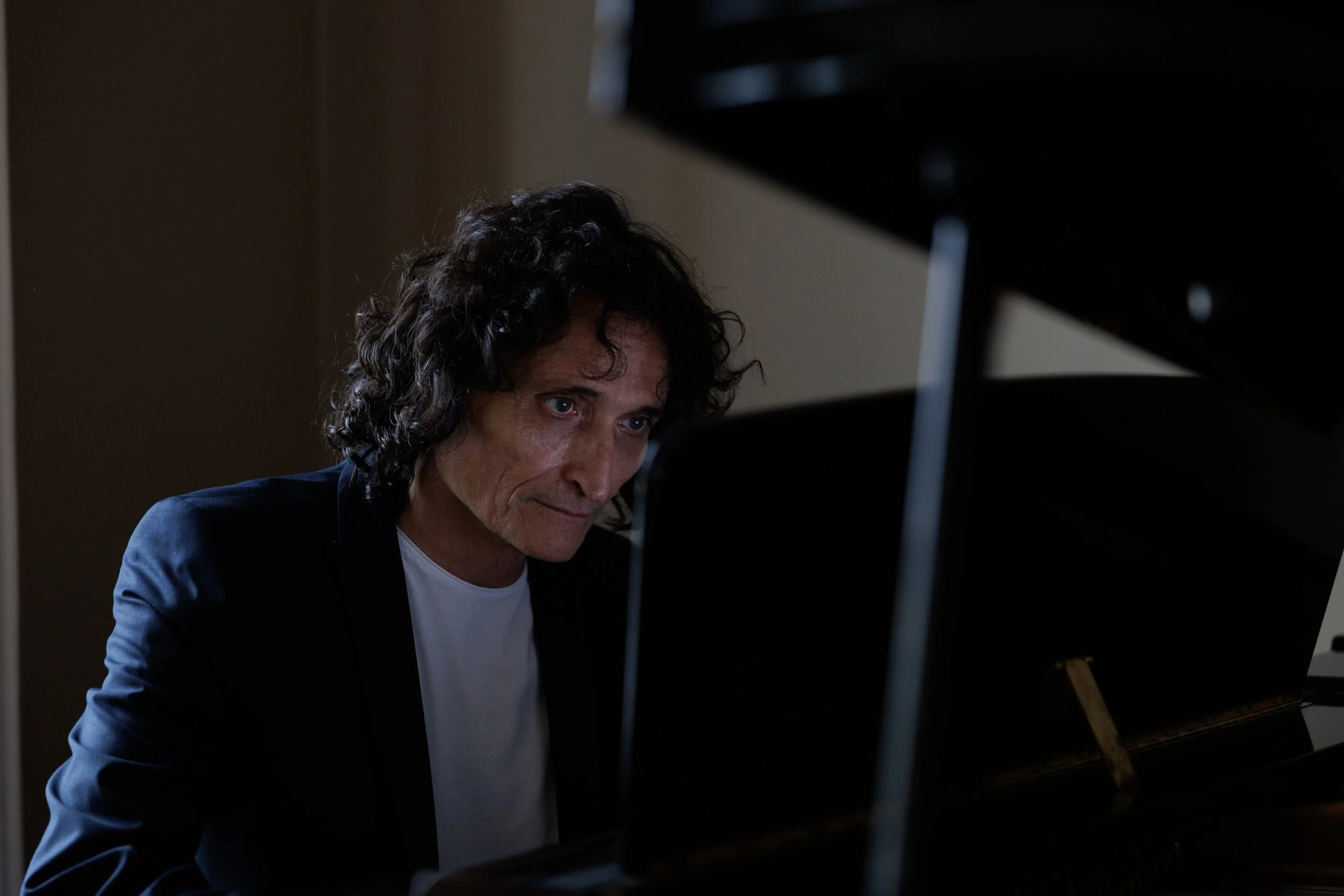 Un homme avec des cheveux frisés et une expression concentrée joue du piano en regardant l'instrument.