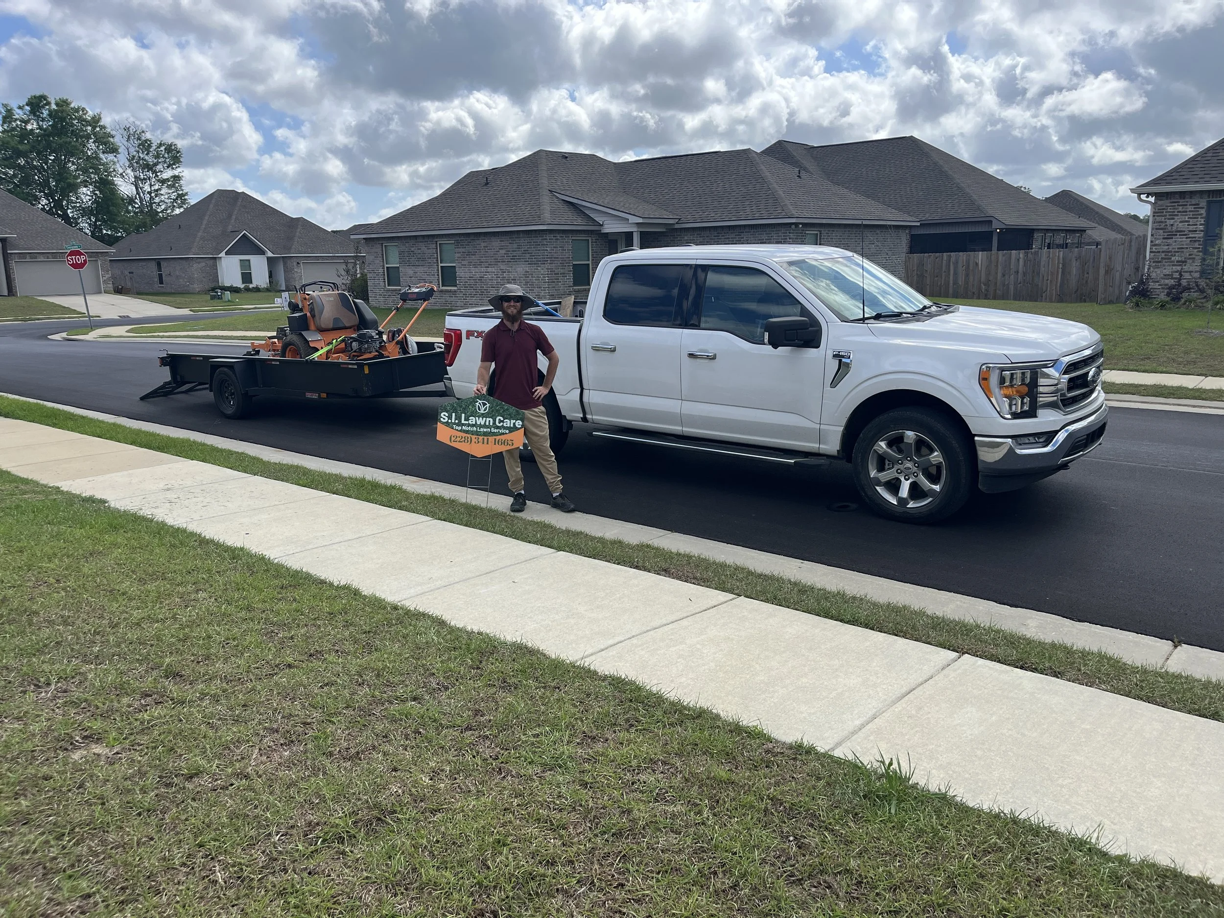 Professional lawn care truck and trailer with a man in front of a residential yard in gulfport, Ms