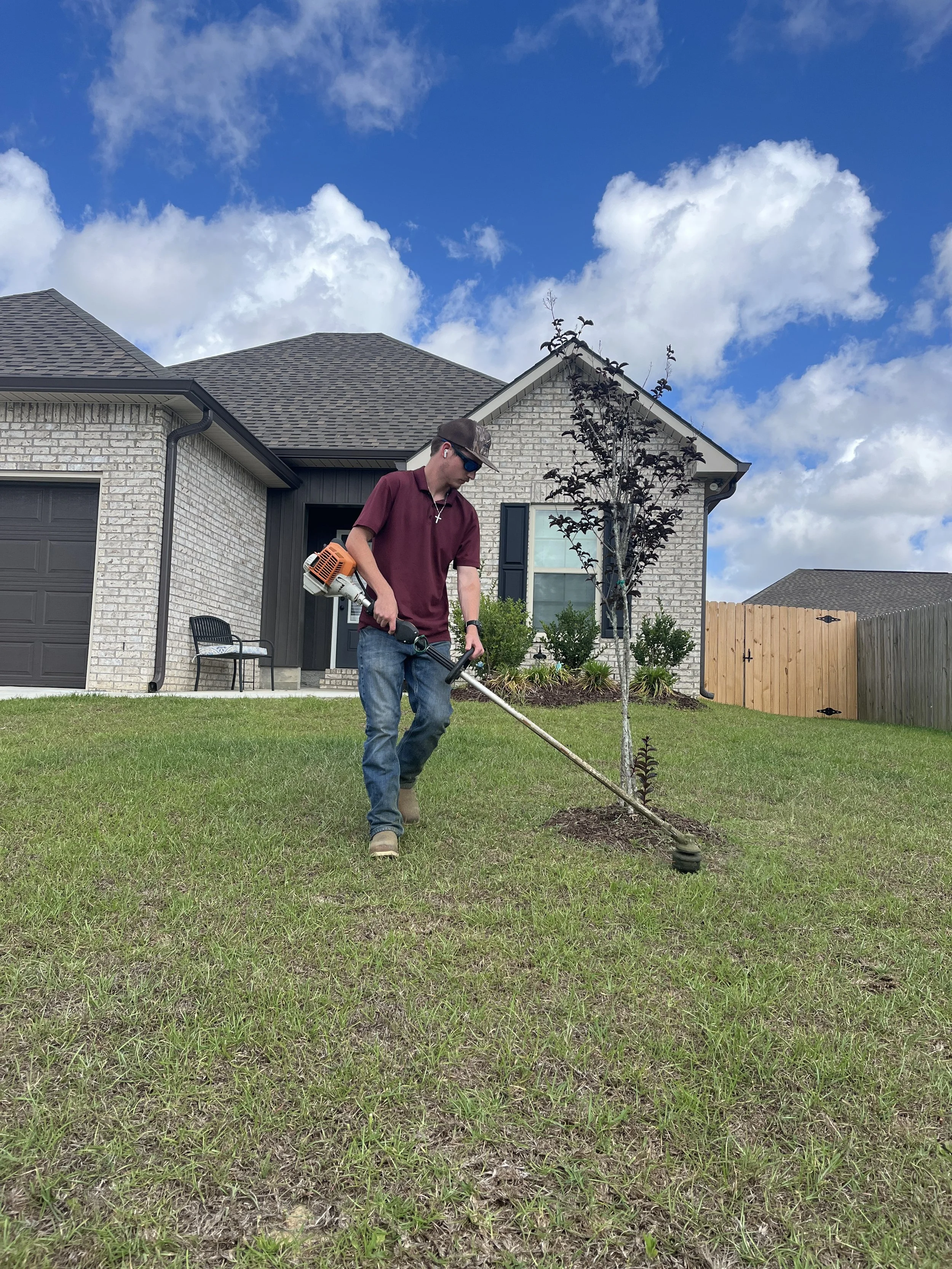 Professional weed trimming and lawn maintenance service in Gulfport MS with a landscaping crew member string trimming around a residential property for a clean finished appearance.