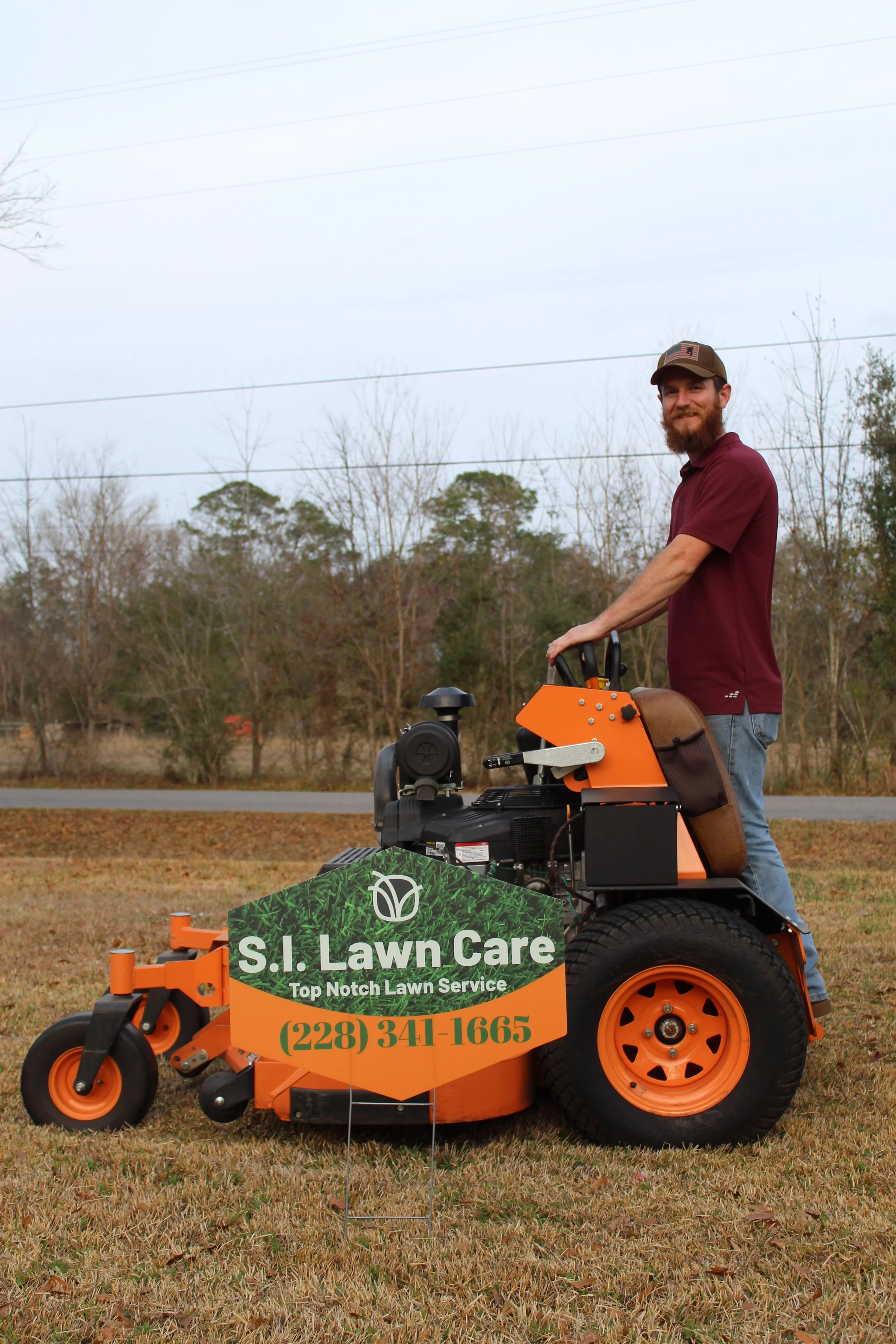 S.I. Lawn Care owner on a professional lawnmower with S.I. Lawn Care sign on the side, on a lawn in Gulfport, Ms with trees and 
power lines in the background.