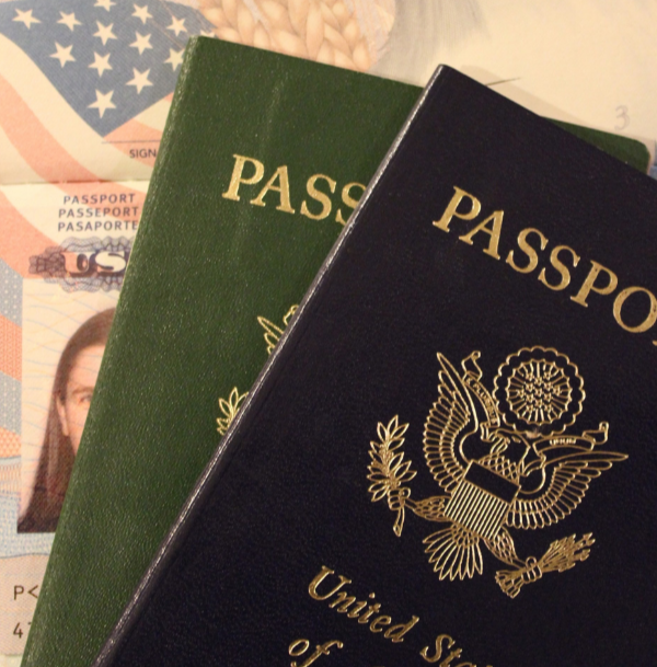 Two U.S. passports, one green and one navy blue, laying on top of a partially visible U.S. passport application form and a passport photo sheet.