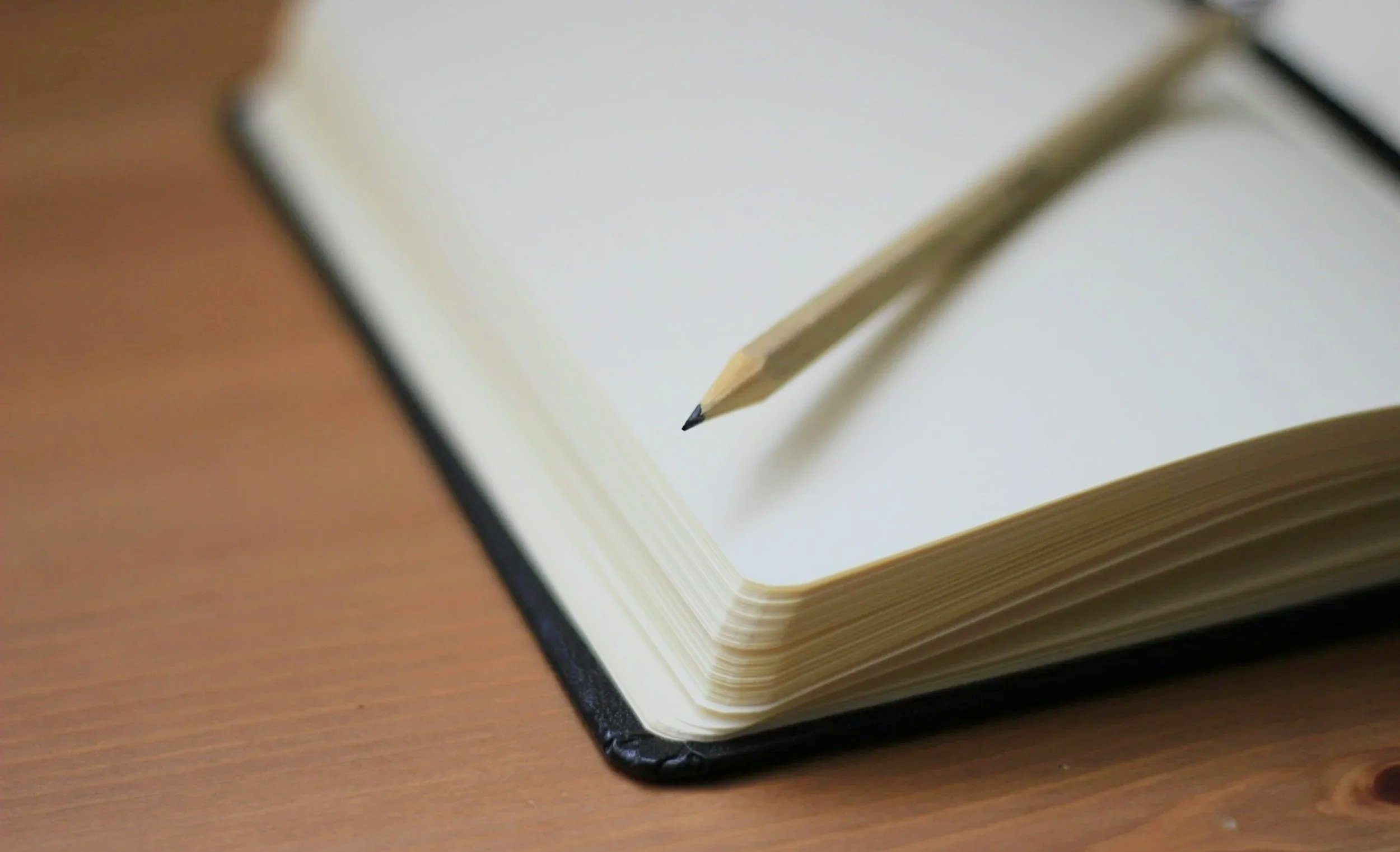 Open notebook with blank pages and a pencil resting on top, placed on a wooden surface.