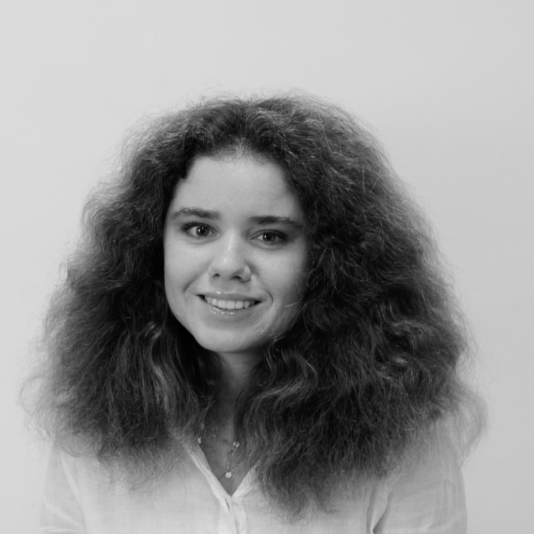 A woman with curly, voluminous hair smiling at the camera, wearing a light-colored top.