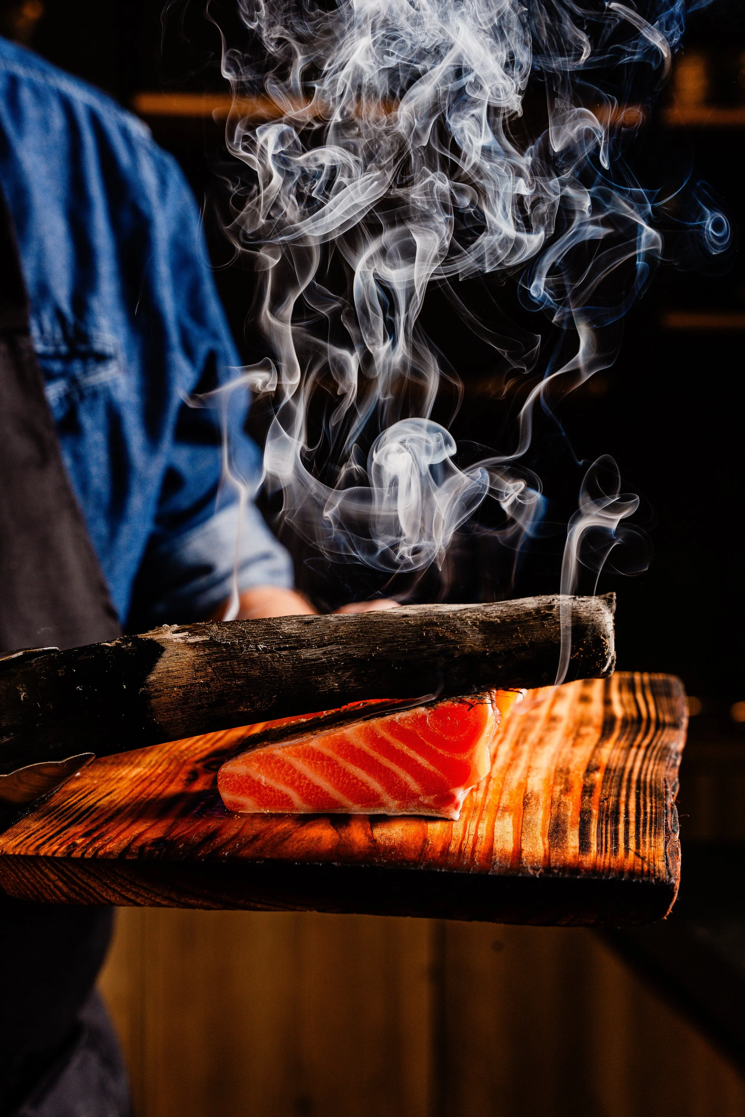 Een stuk gerookte zalm ligt op een houten snijplank, met rook die opstijgt boven de zalm.