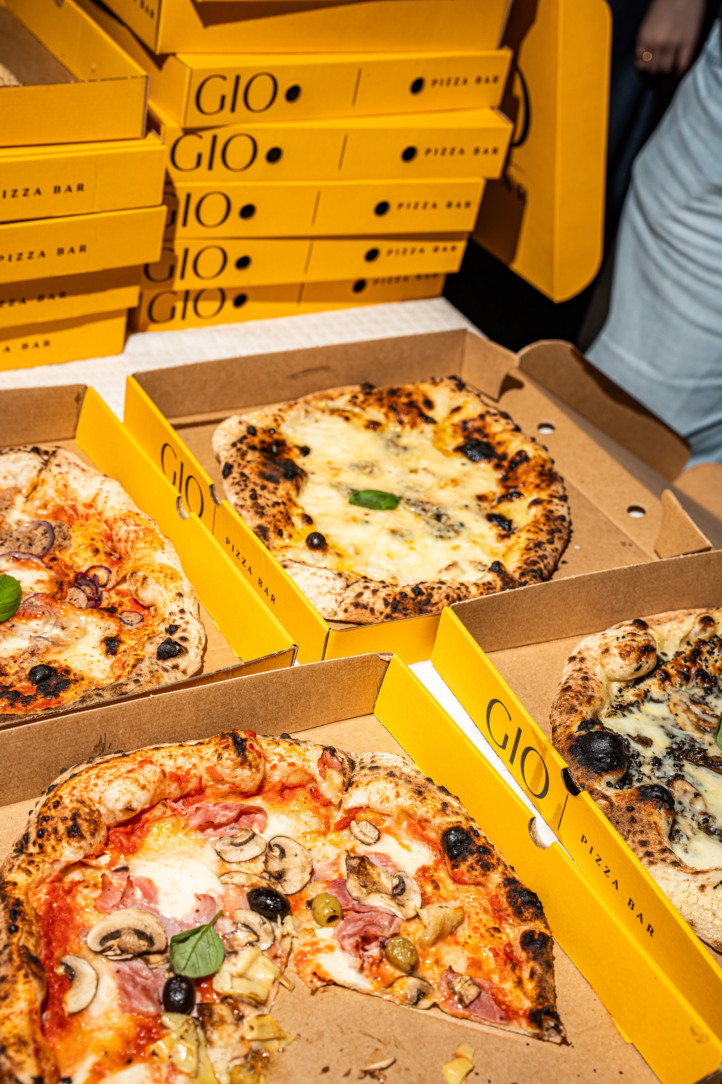 Gezicht op verschillende pizza's in roze dozen, met zwarte en groene olijven, champignons en ham, en een stuk gesneden pizza.