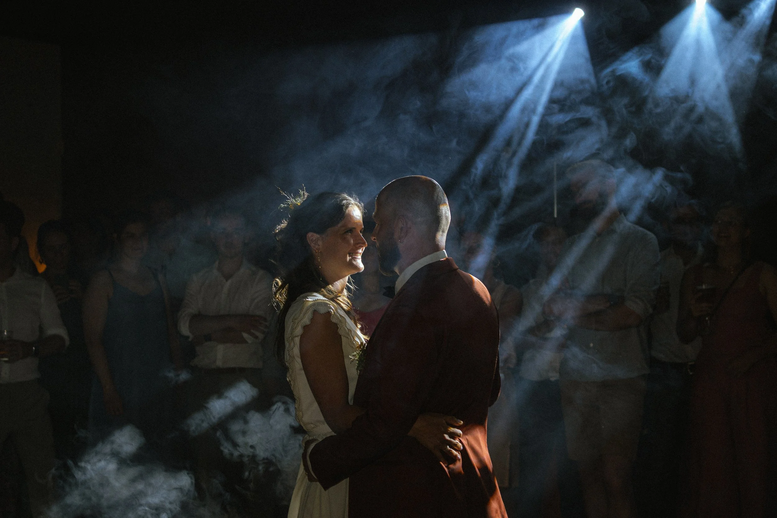 Een bruiloftsvoorbeeld met een stel dat danst onder een donkere hemel met lichte lichtstralen en rook of mist op de achtergrond.
