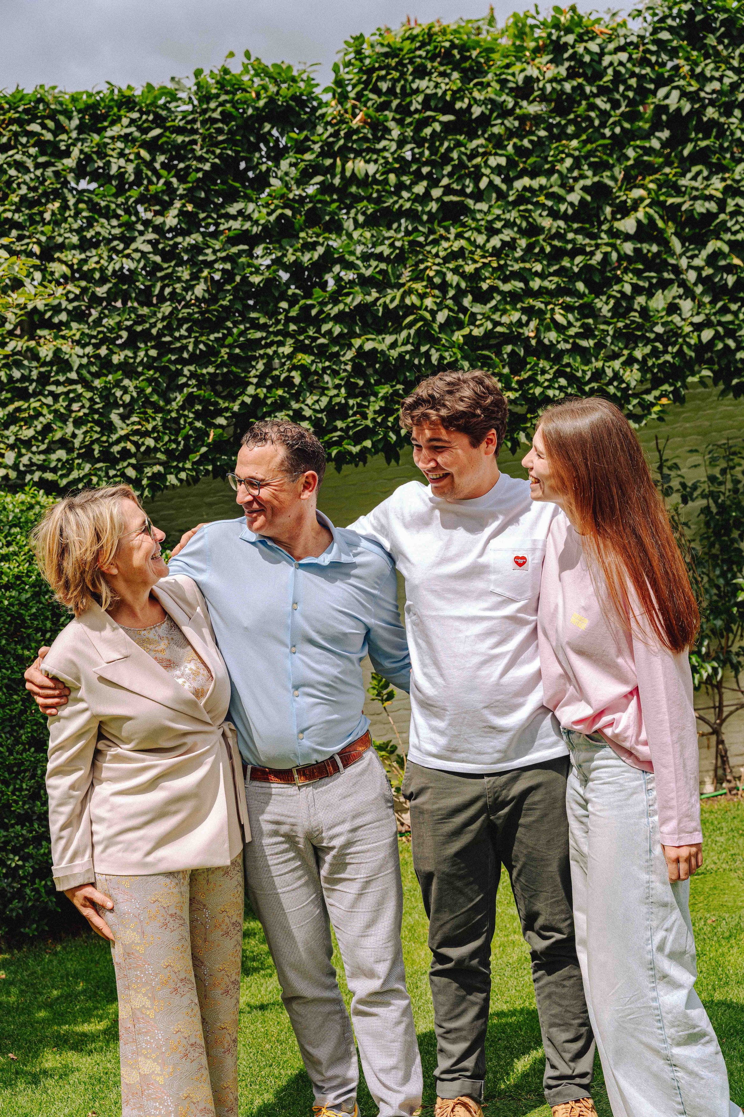 Vijf mensen die samen lachen en elkaar omhelzen in een groene tuin.