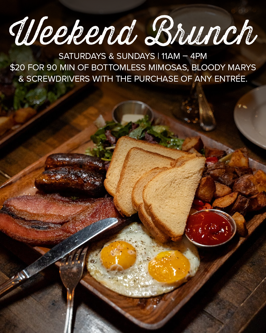 A wooden platter of breakfast food including two sunny side up eggs, slices of toast, bacon, sausage, roasted potatoes, a small salad, and a side of ketchup, with promotional text for weekend brunch.
