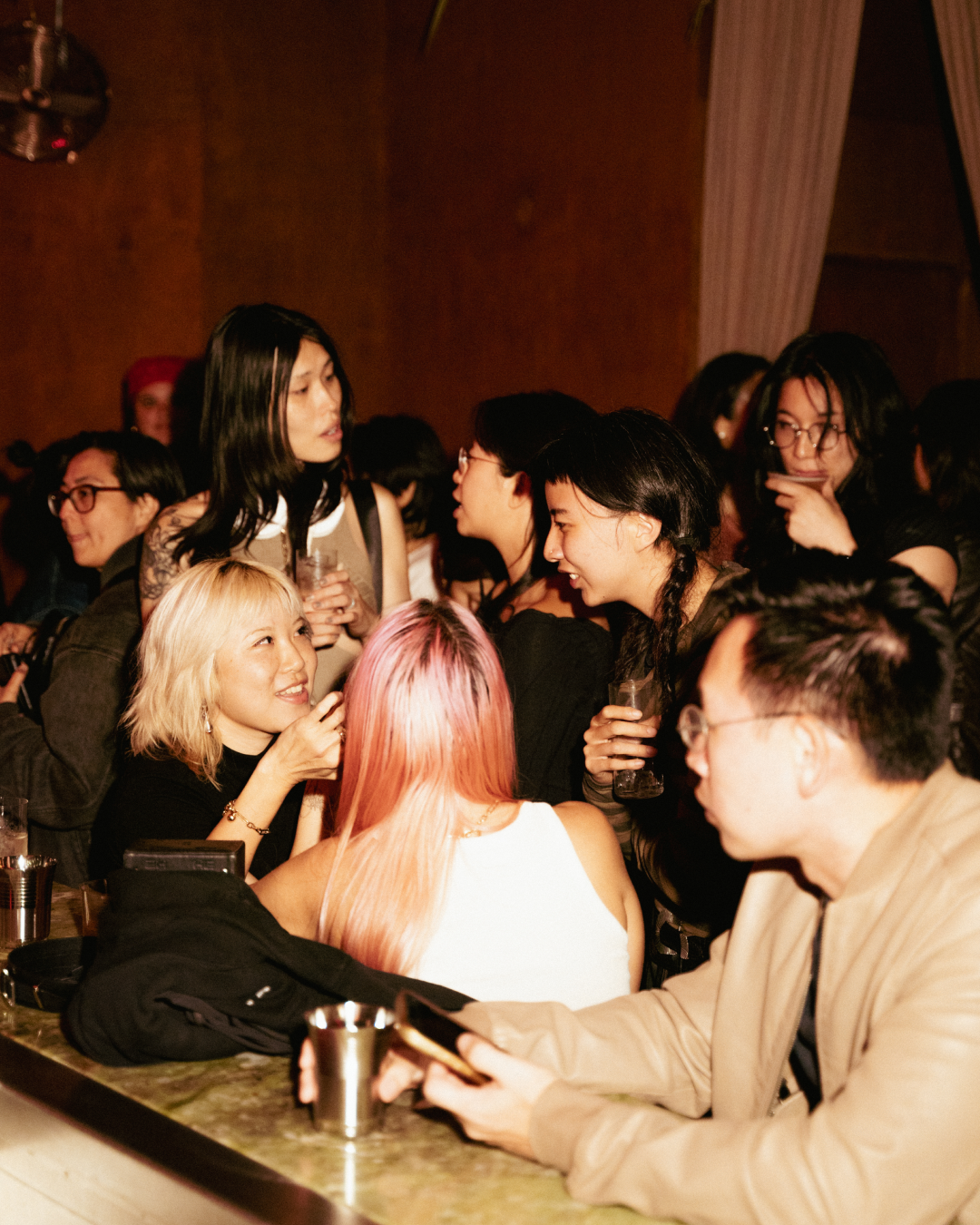 Group of young adults socializing at a bar or nightclub with warm lighting.