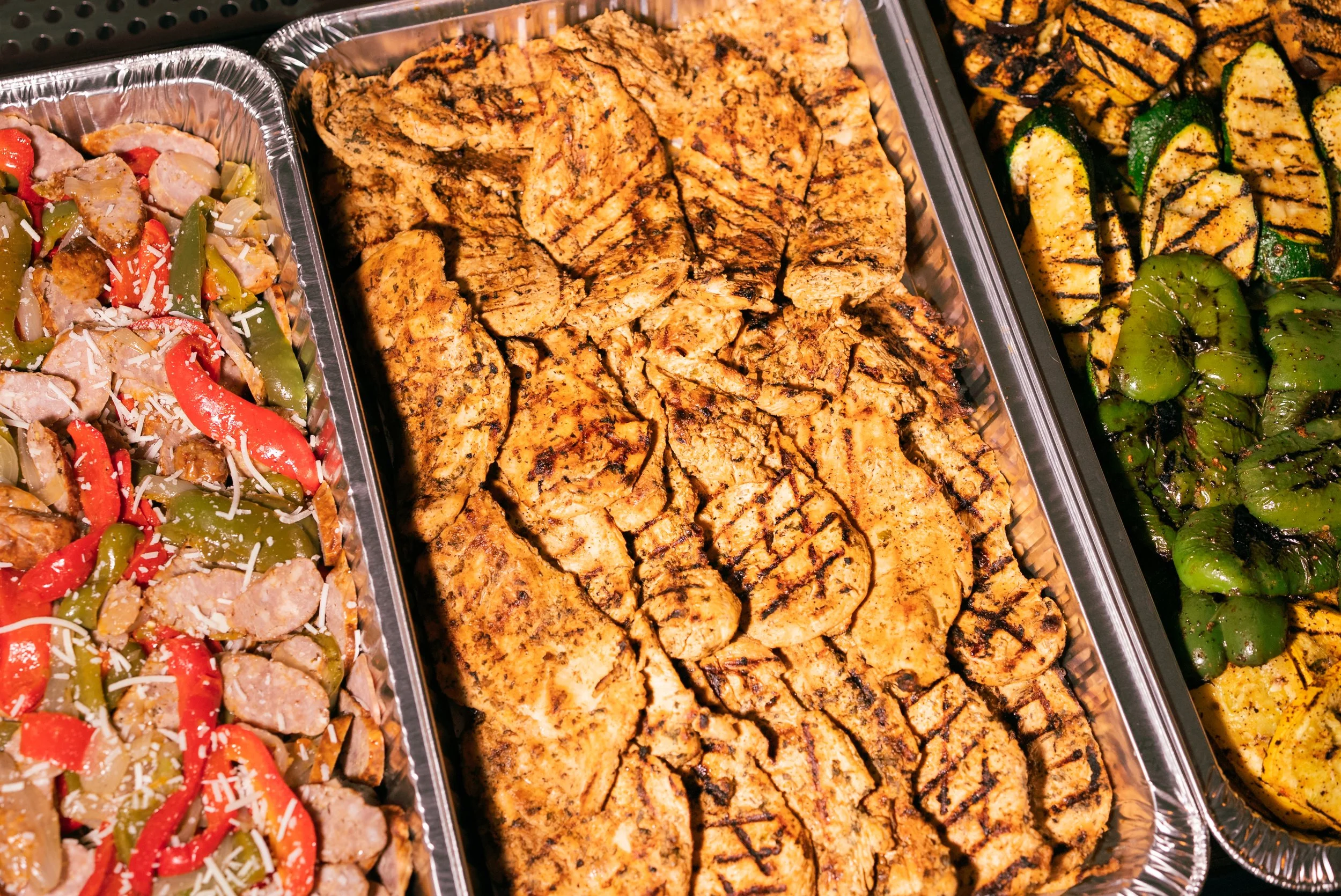 Tri-color grilled chicken, grilled zucchini, and grilled green peppers in catering trays.