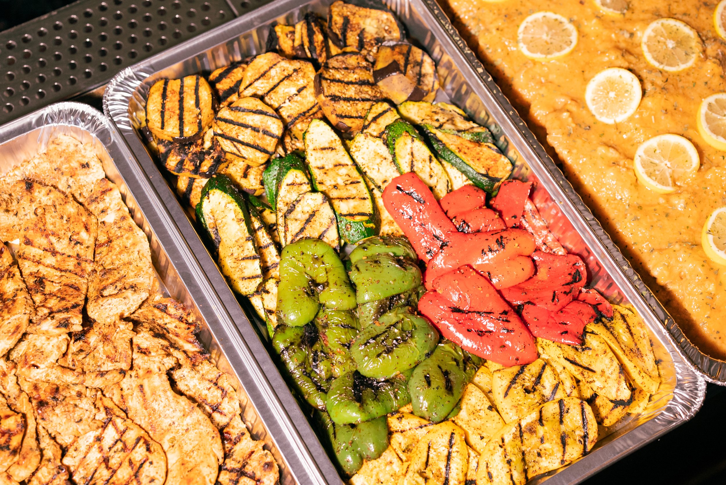 Assorted grilled vegetables and skewers, including zucchini, red peppers, and yellow squash, on a buffet tray.