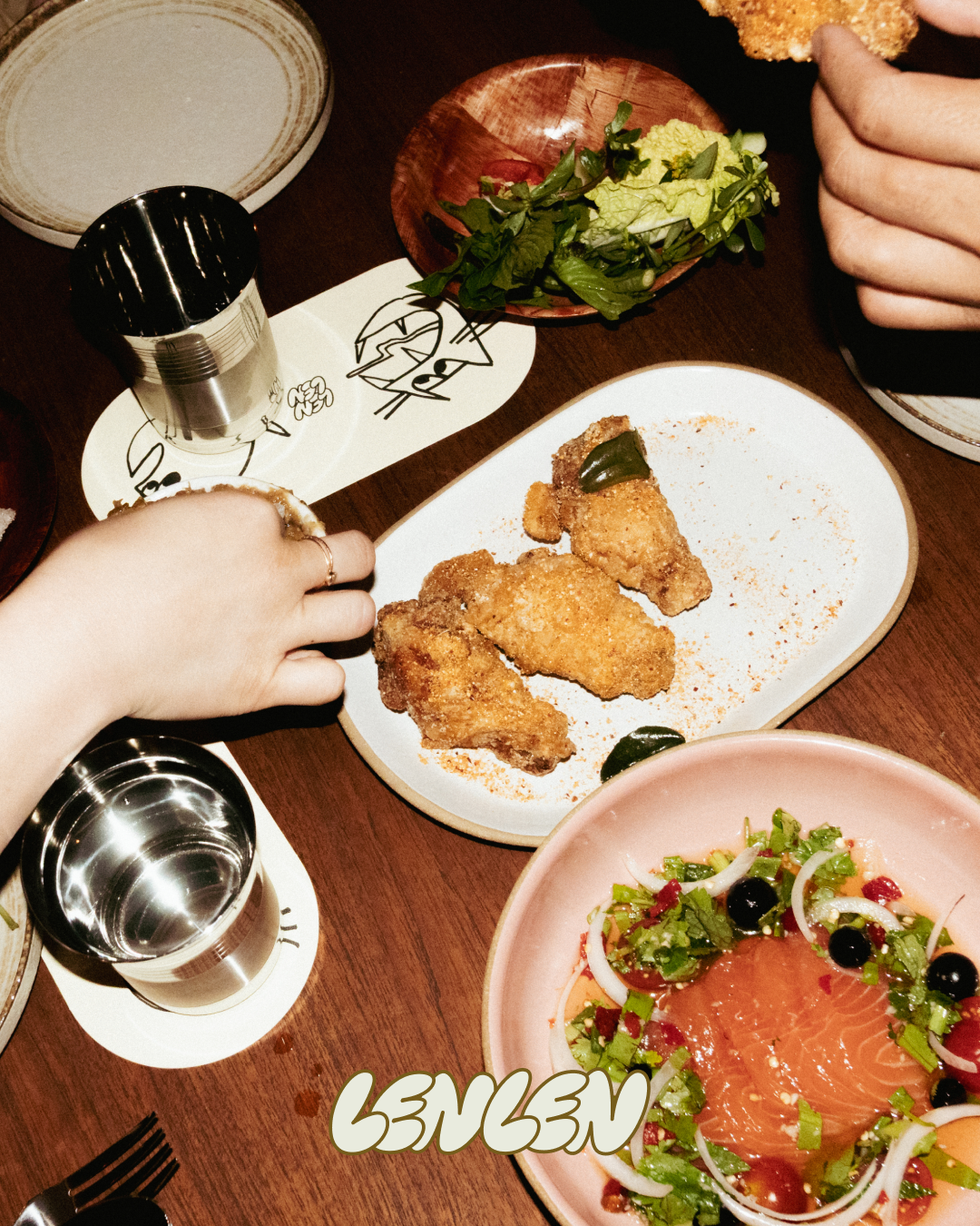 Plate of fried chicken with two pieces garnished with jalapeños on a table, alongside a salad with mixed greens, sliced vegetables, and smoked salmon, and two glasses of water.