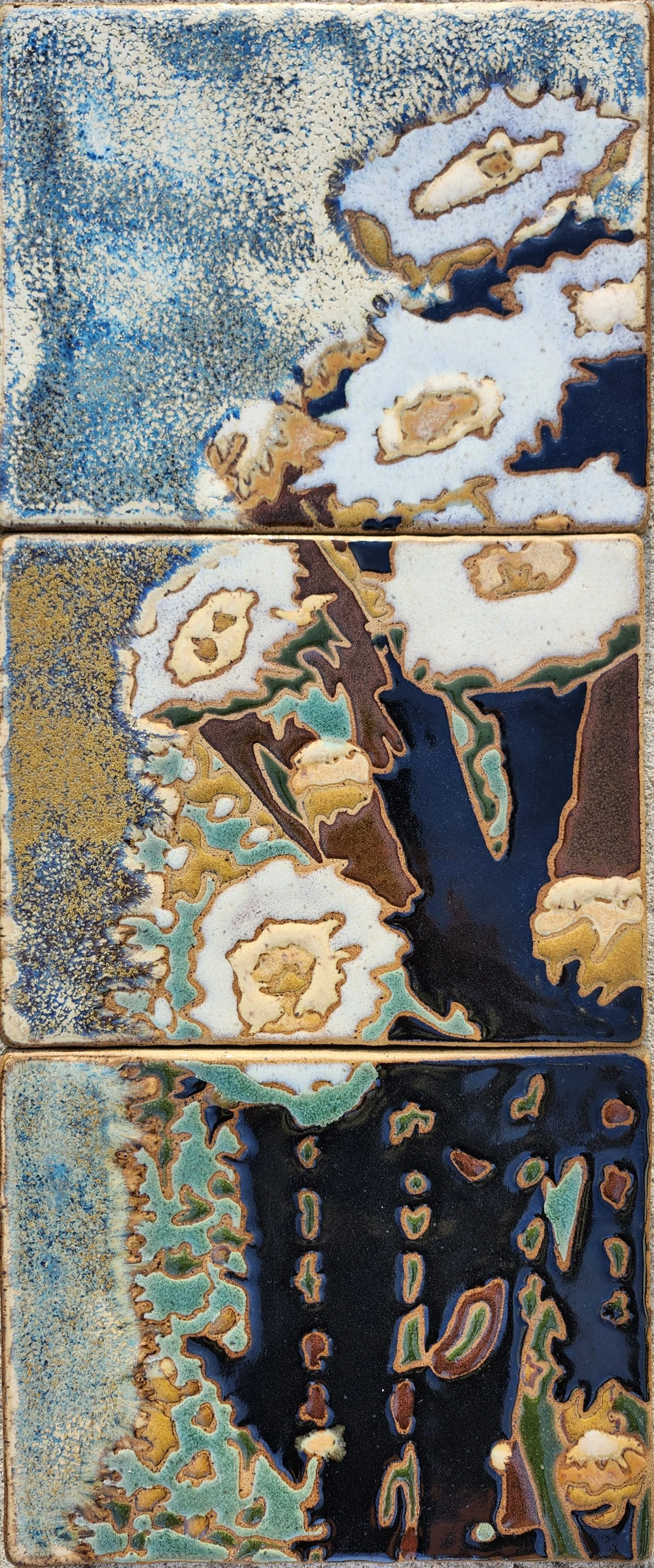 Three ceramic tiles with abstract, colorful patterns resembling trees, water, and natural landscapes.
