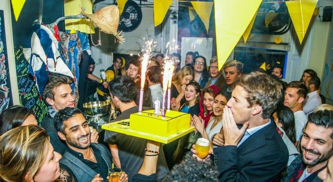 People celebrating with a cake and sparklers in a decorated party room.