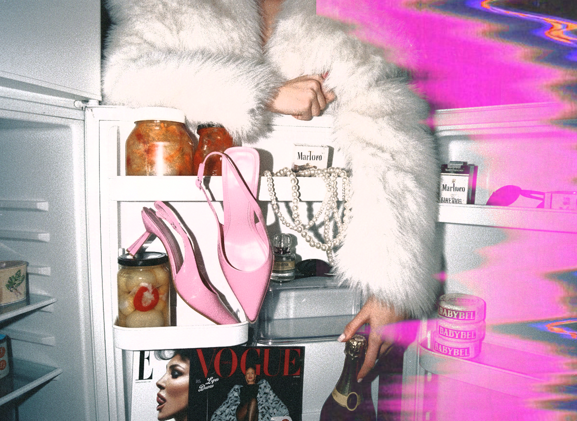 A person in a white faux fur coat reaching into an open refrigerator filled with jars, pink high-heeled shoes, jewelry, a Vogue magazine, and food items. The door has pink and purple hues and the image has a distorted, glitchy effect.