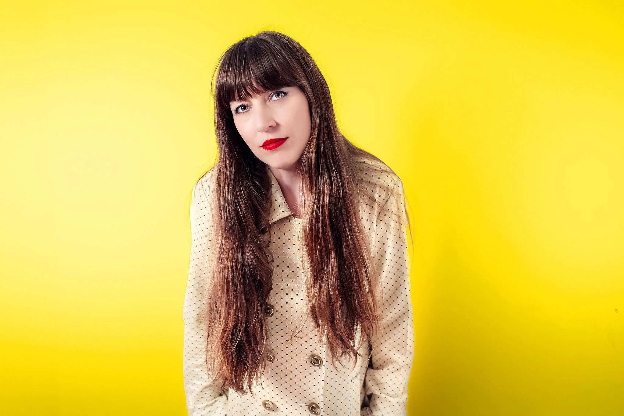 Fashion self-portrait of Heather Bays in a vintage yellow blazer dress against a bold yellow background, wearing red lipstick in soft even studio light.