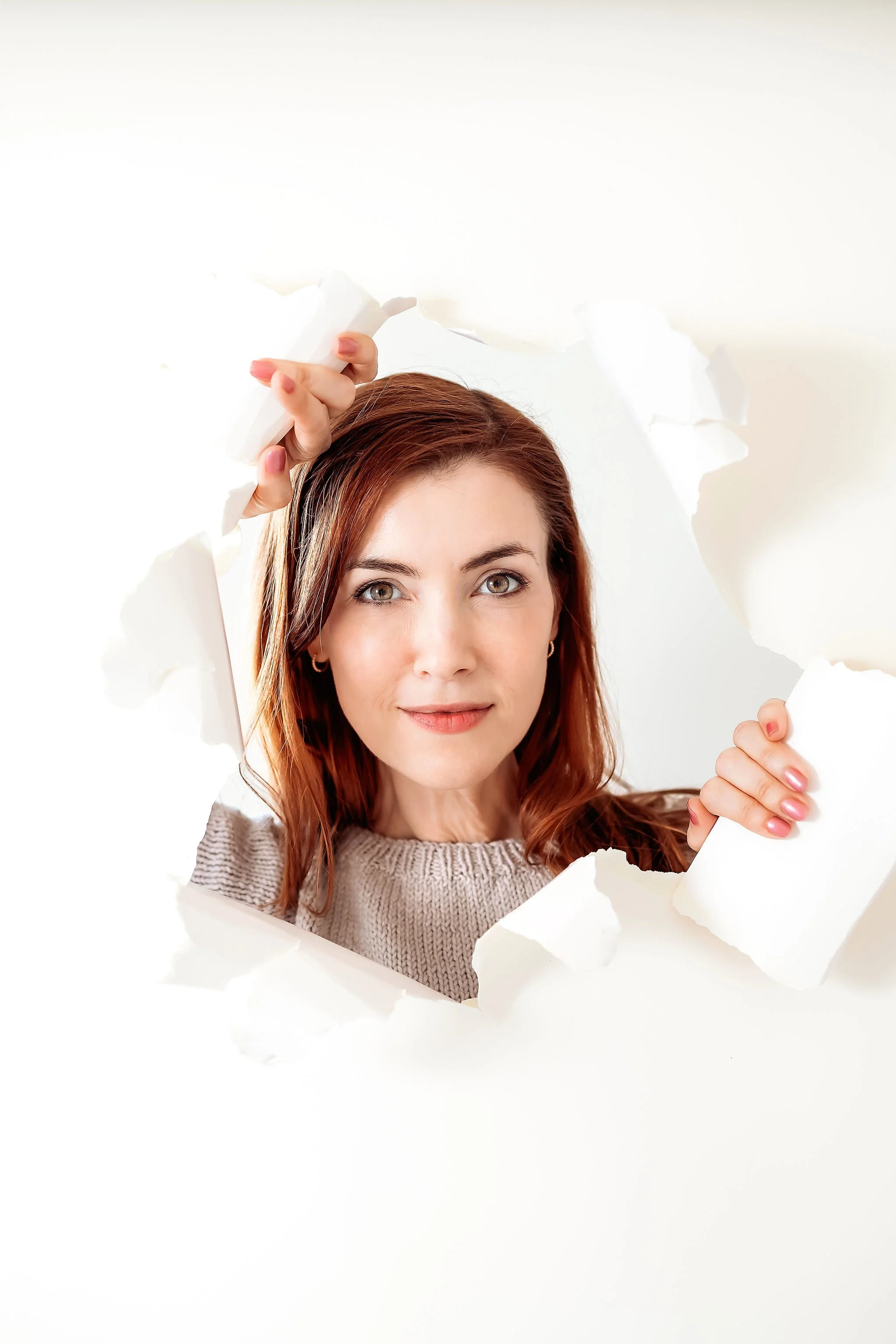 Woman with red hair breaking through white paper for creative portrait photography