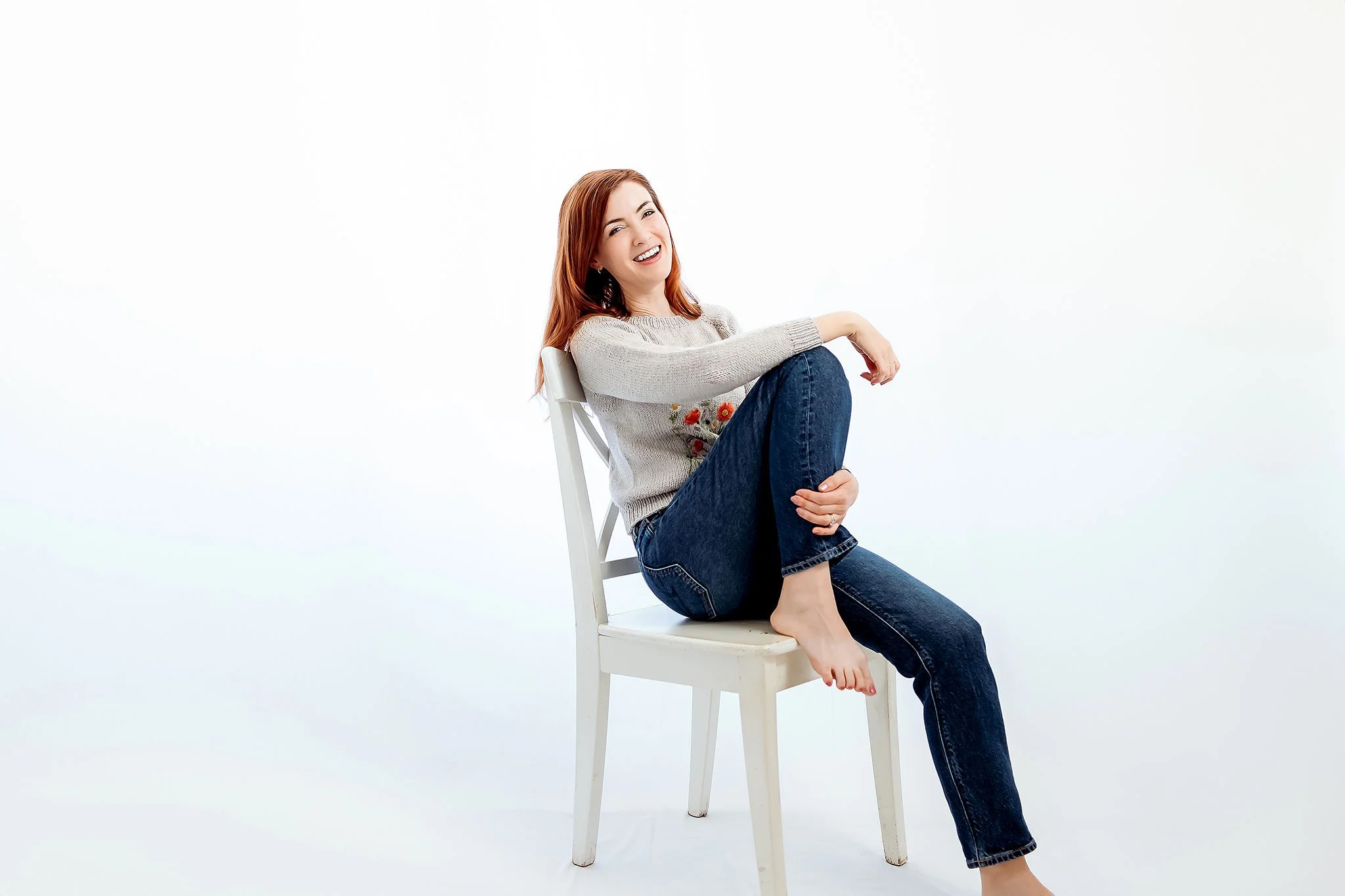 Woman sitting on white chair smiling during personal branding photography session