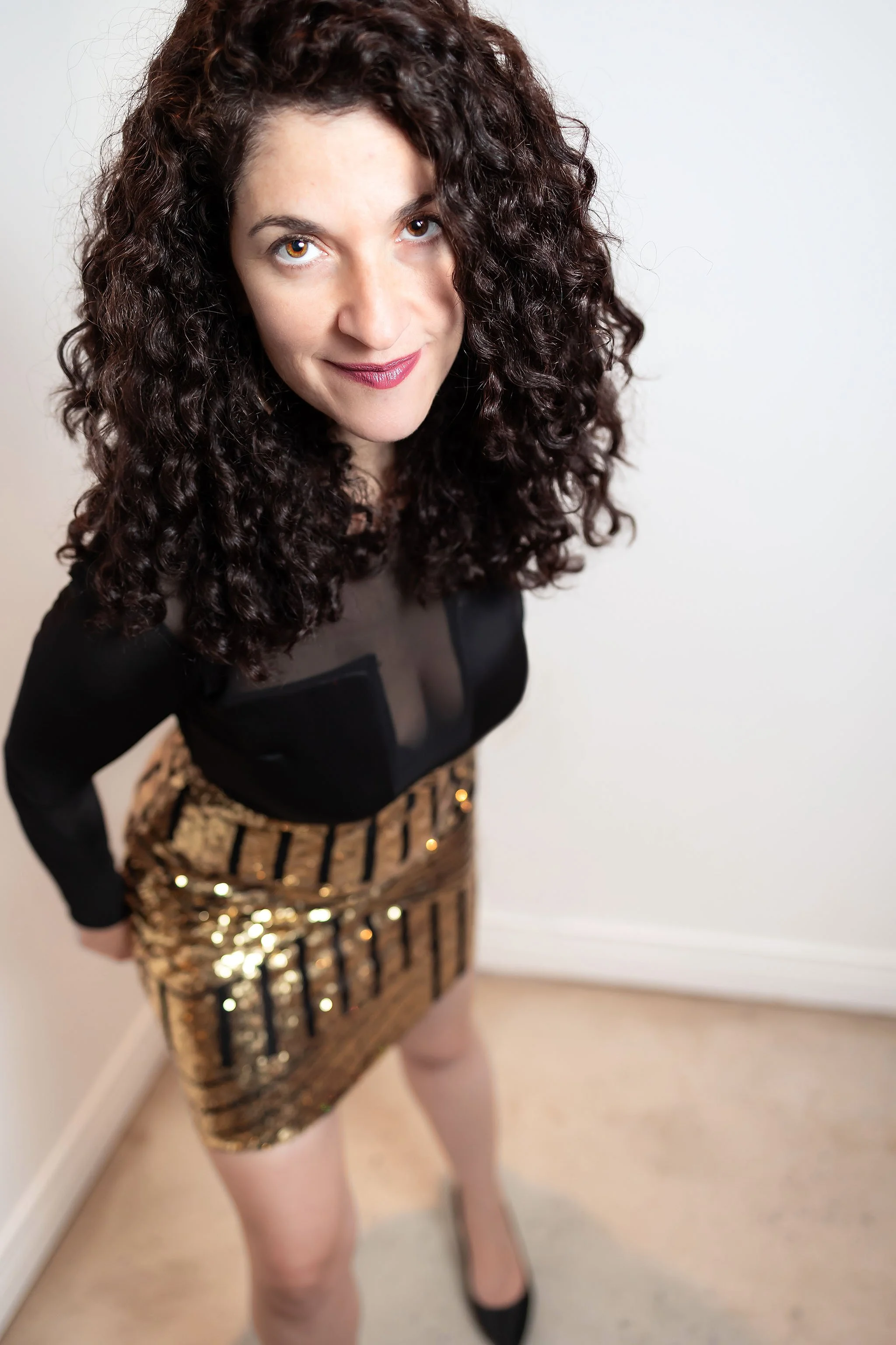Woman with curly hair wearing black top and gold skirt in editorial portrait