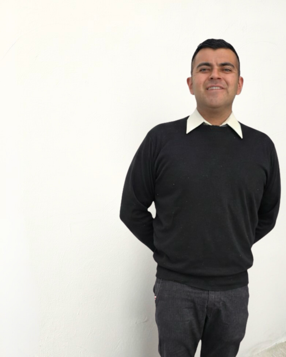 Hombre de pie con ropa formal, sonrisa y fondo blanco.