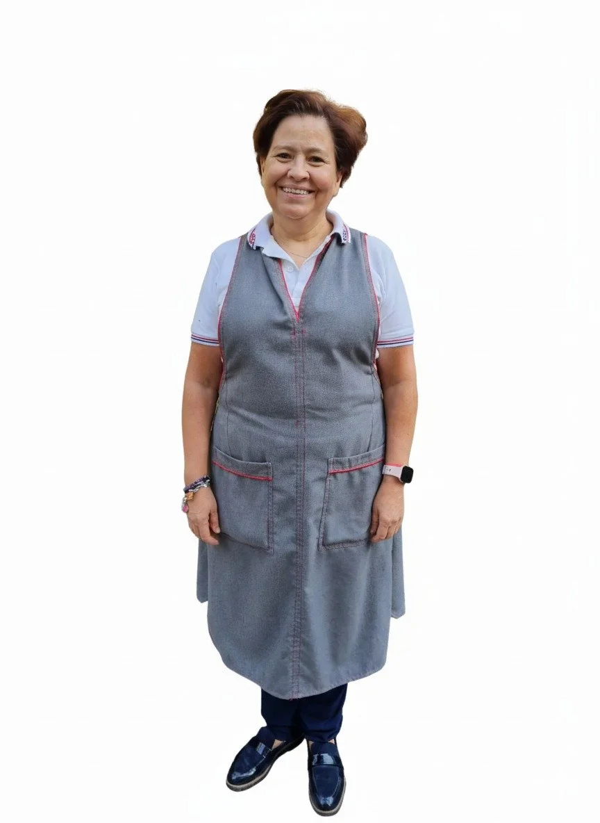 Mujer sonriendo, usando uniforme gris con falda y camiseta blanca, calzado oscuro, accesorios y reloj. Fondo blanco.
