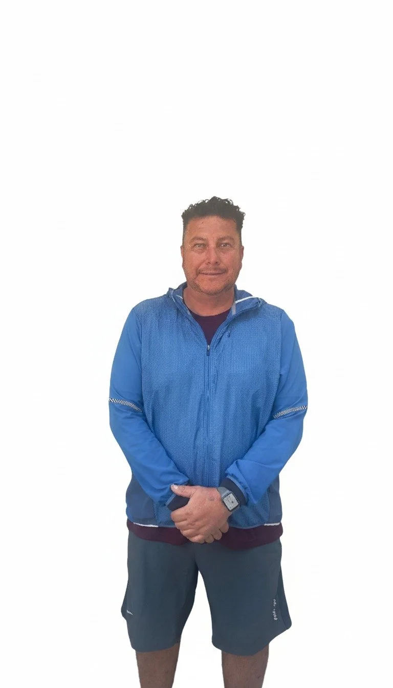 Hombre con chaqueta azul y pantalones cortos, parado contra fondo blanco.