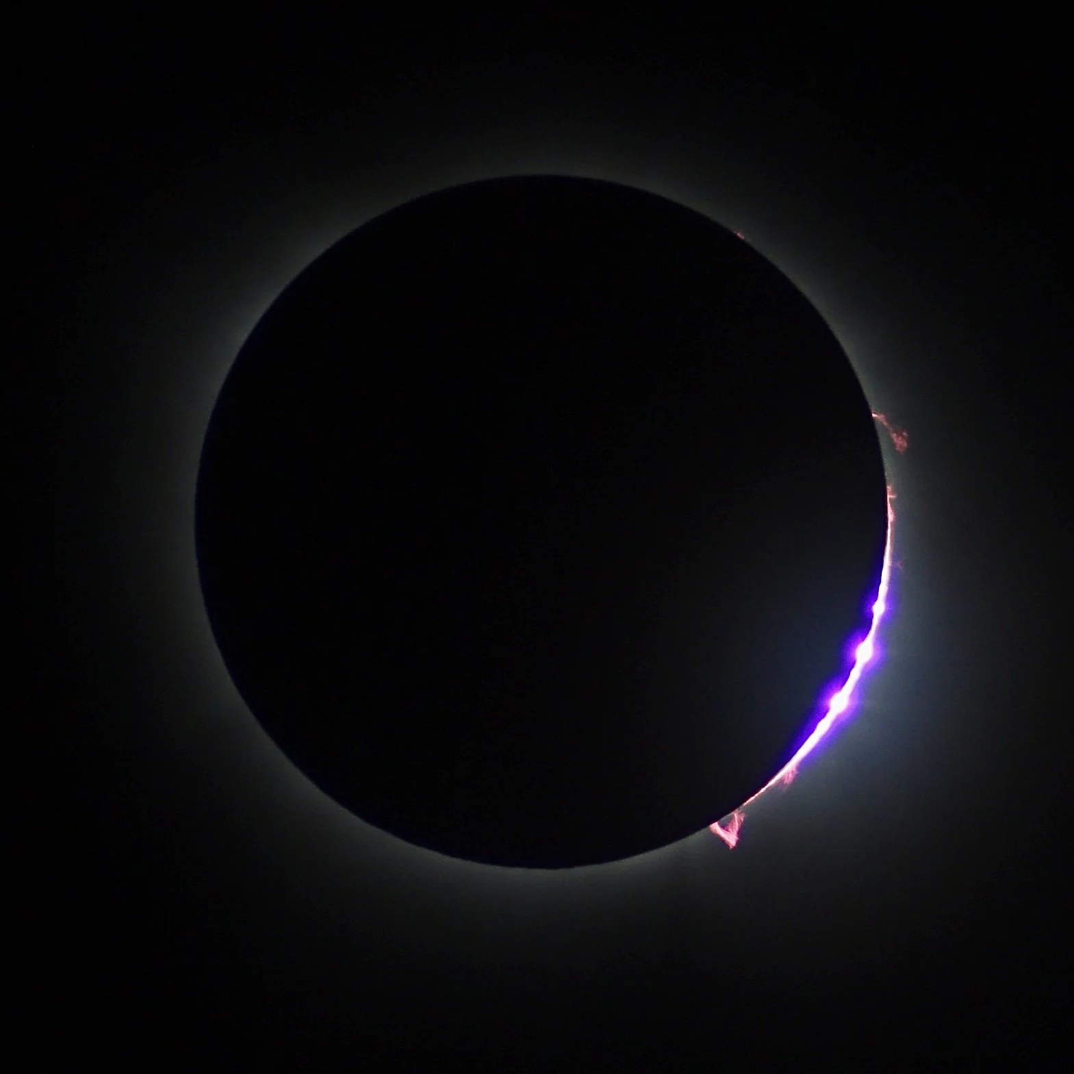 A solar eclipse with the moon covering the sun, a bright corona is visible around the edges with purple and pink lightning-like streaks on the lower and right edges.