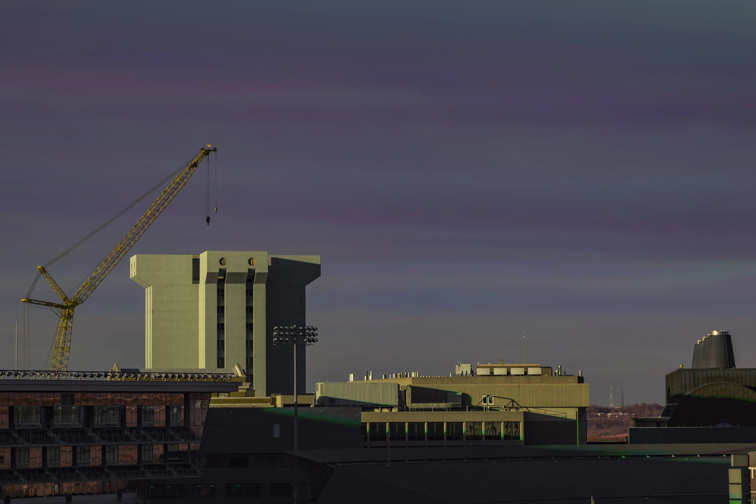 City skyline with a large construction crane and tall buildings under a colorful sky.