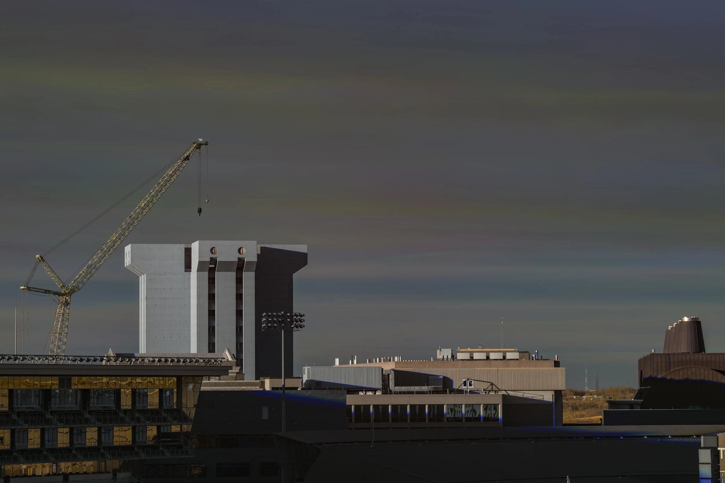 City skyline featuring the top of a modern building, construction crane, and cloudy sky.