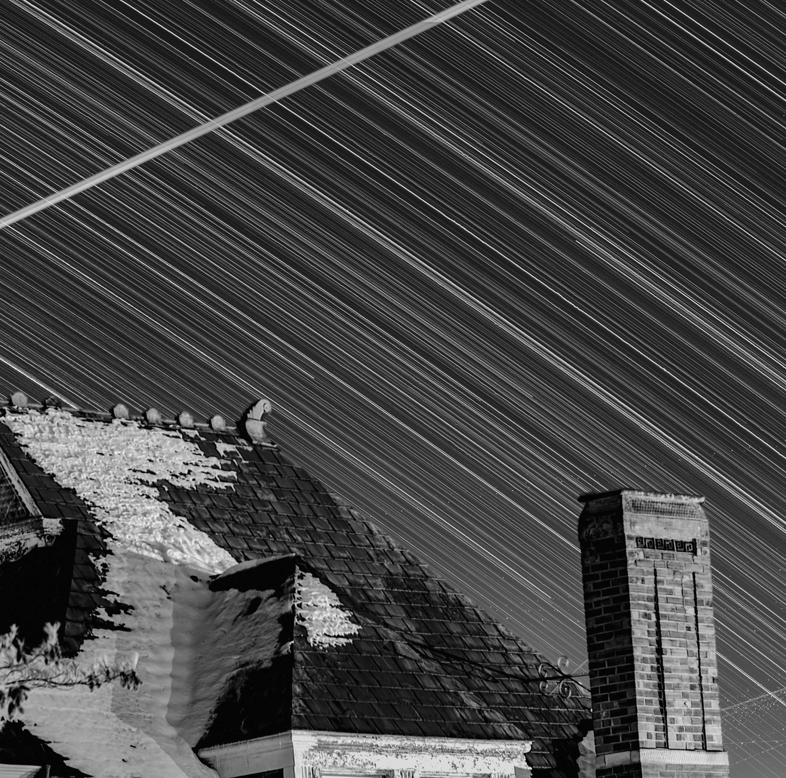 Night sky with star trails above a chimney and part of a snow-covered roof of a house.