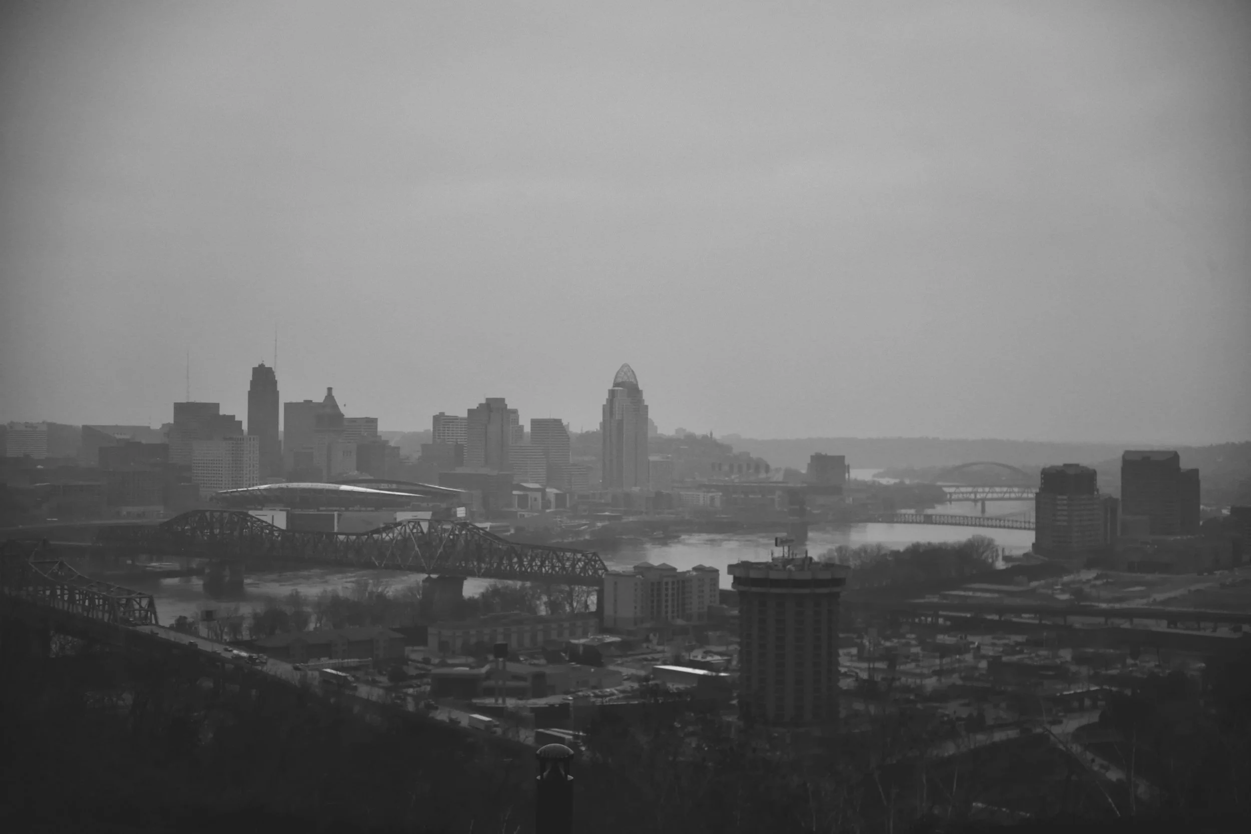 A black and white photo of a city skyline with skyscrapers, bridges over a river, and other buildings in the foreground.