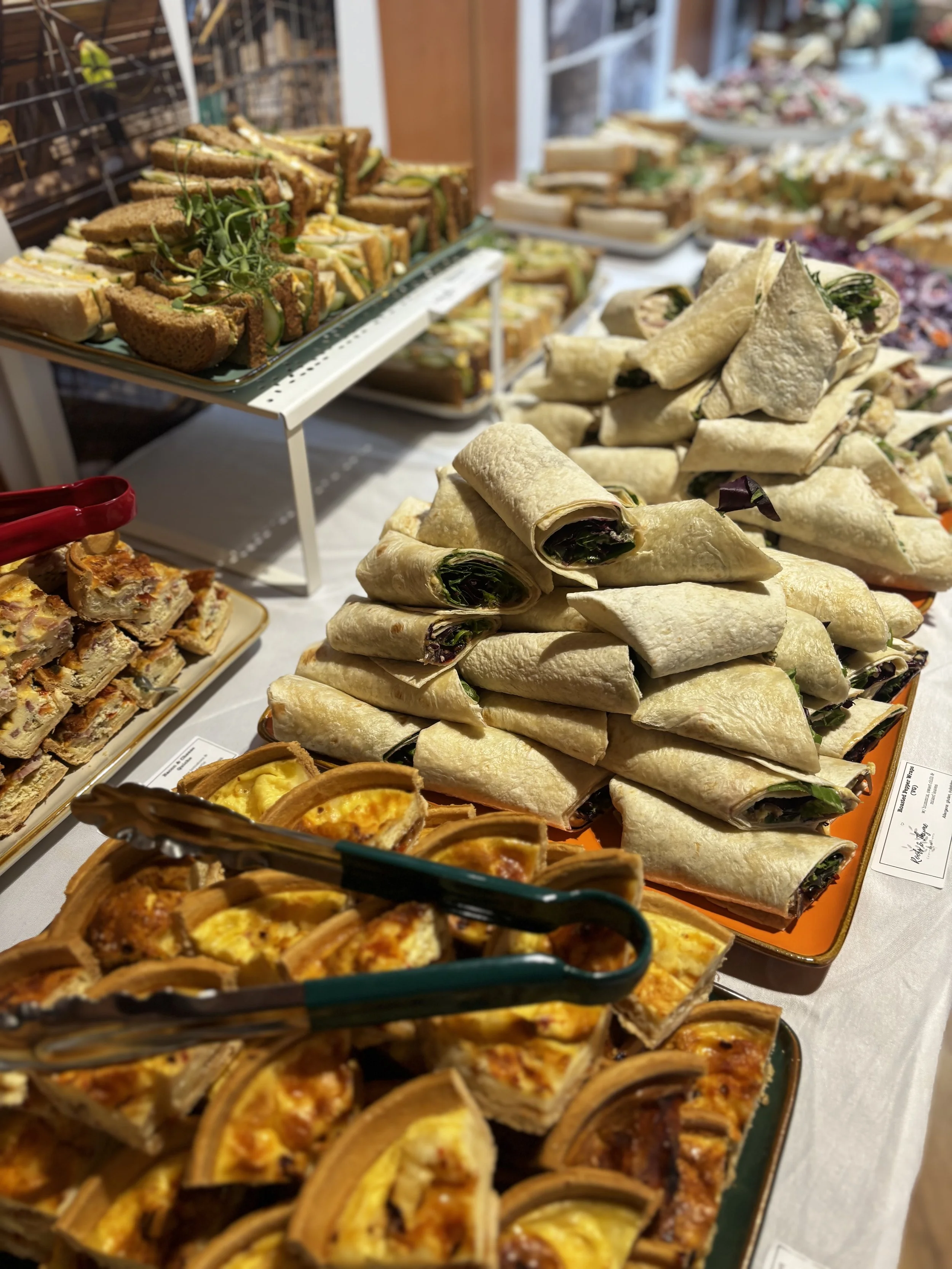 A buffet table with various sandwiches, wraps, and quiches, arranged on trays for a gathering or event.