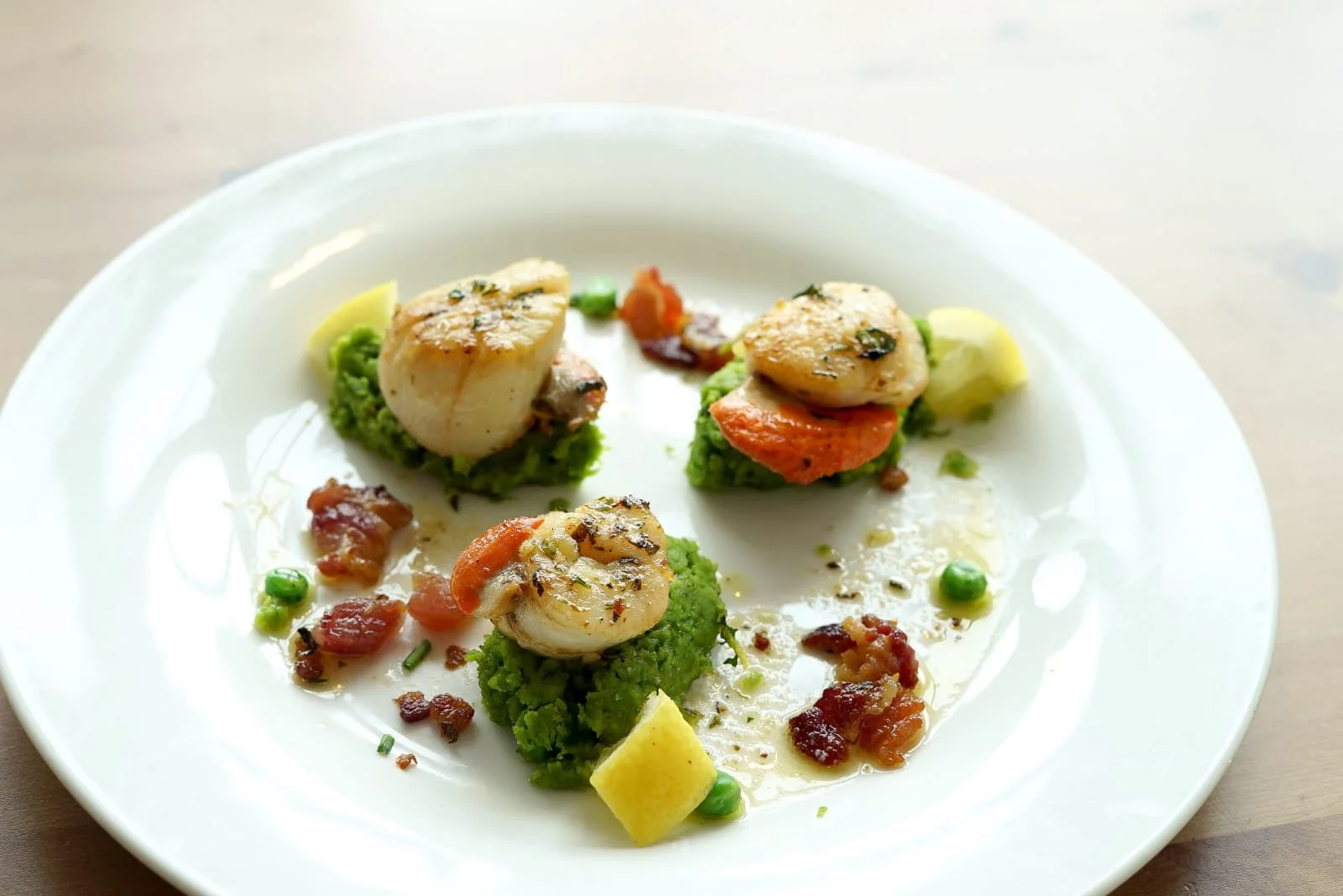 Seafood dish with scallops on a bed of green vegetable mash, garnished with herbs and small sauce drops.